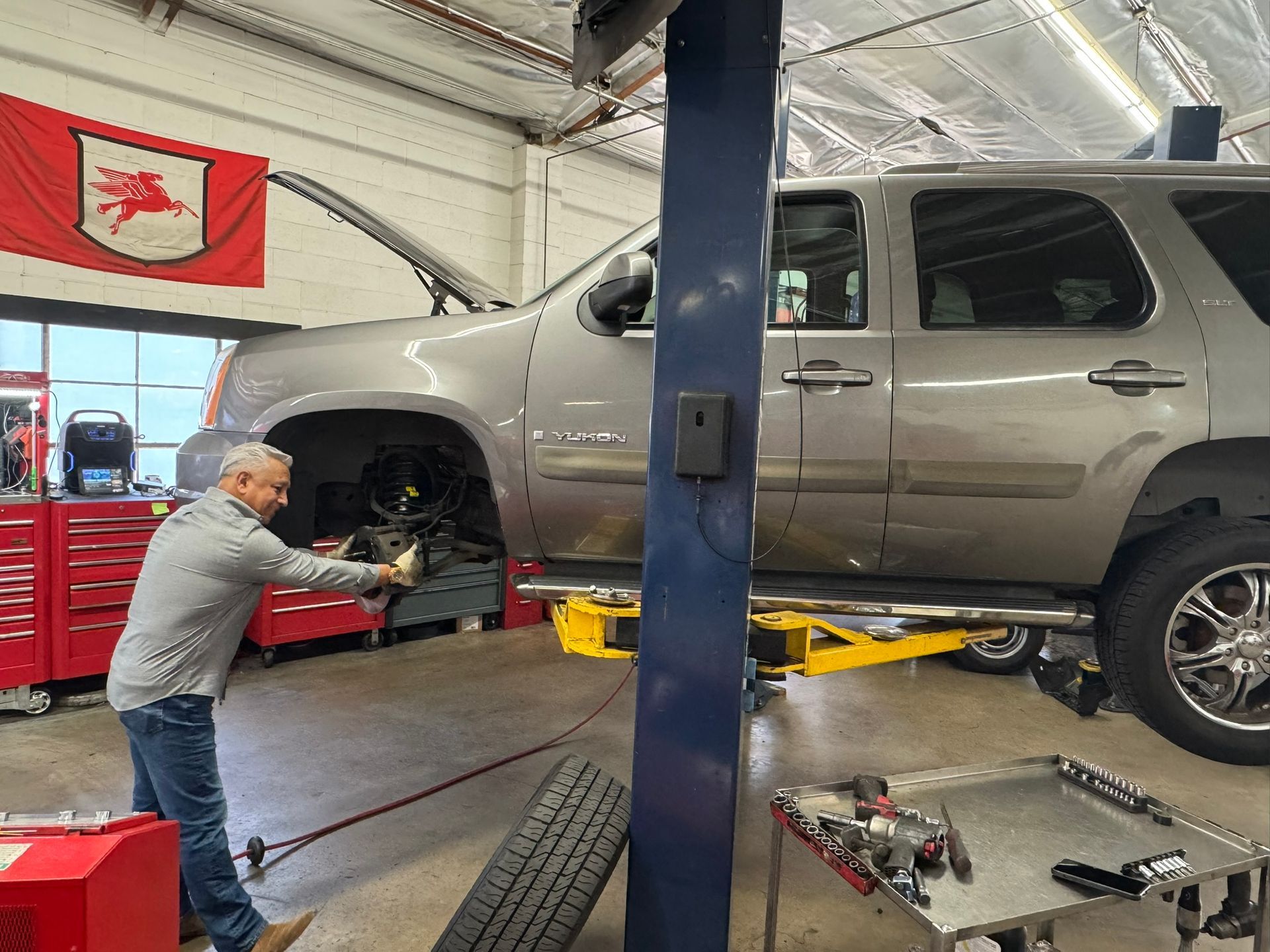 Mechanic working on a silver SUV lifted in an auto repair shop