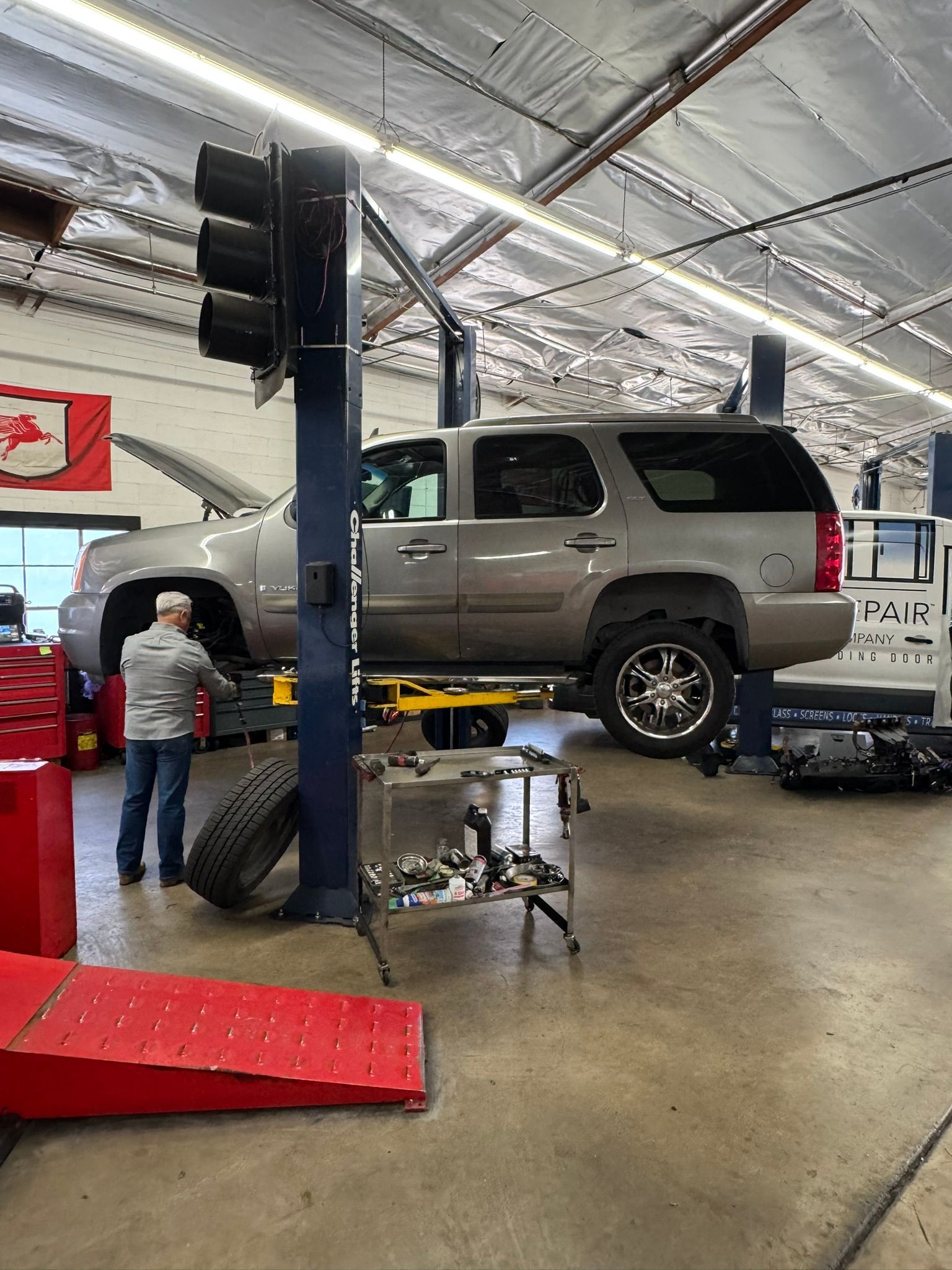 SUV raised on a hydraulic lift in an auto repair shop, with a mechanic working nearby.