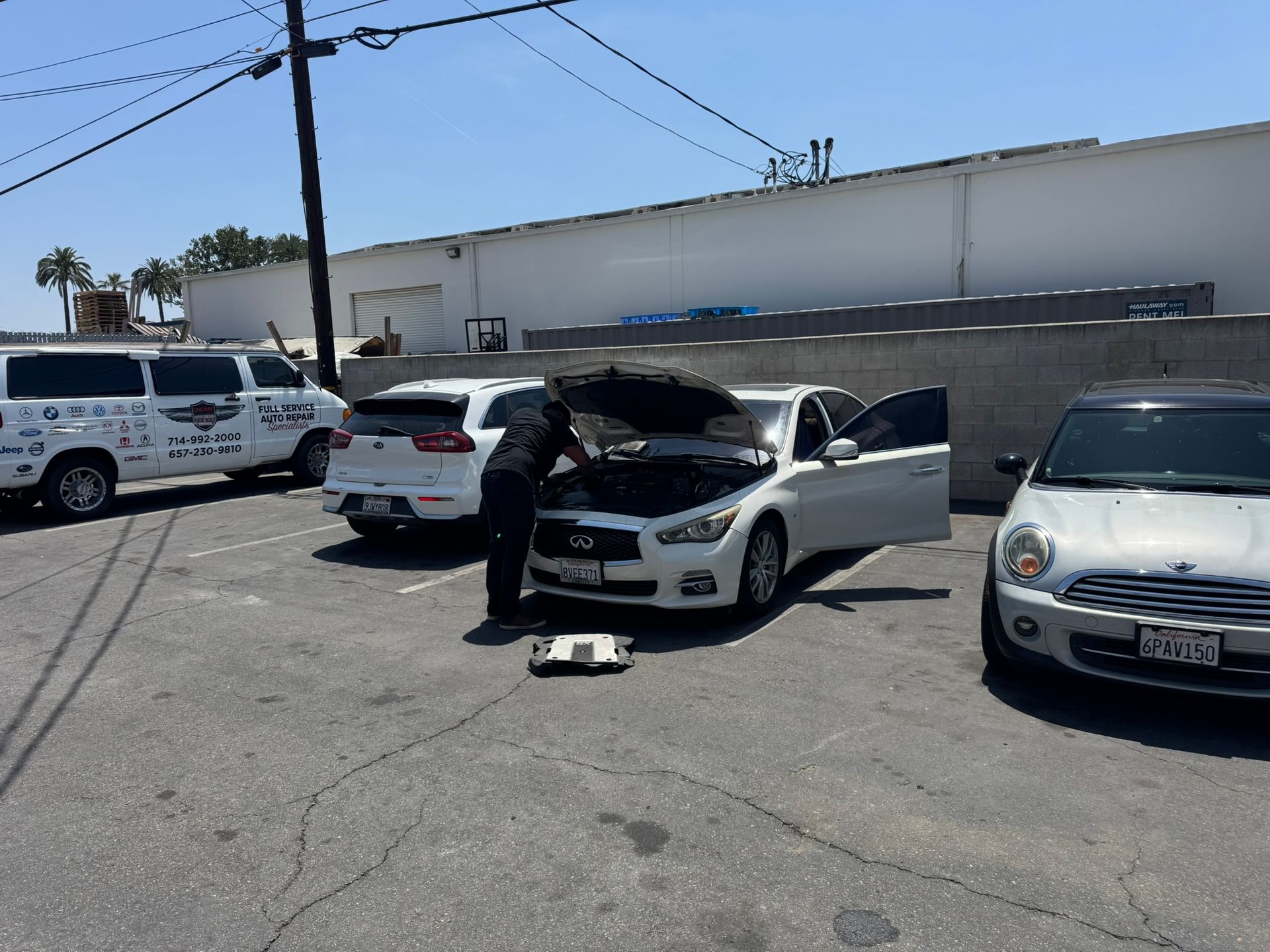 Person checking the engine of a white car in a parking lot beside other vehicles.