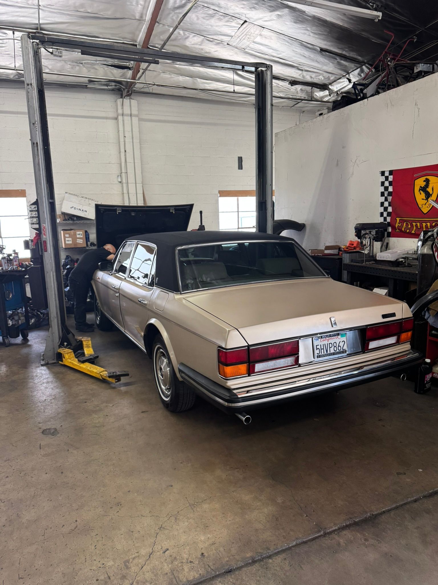 Classic beige convertible in an auto shop bay, with a mechanic working inside the car.