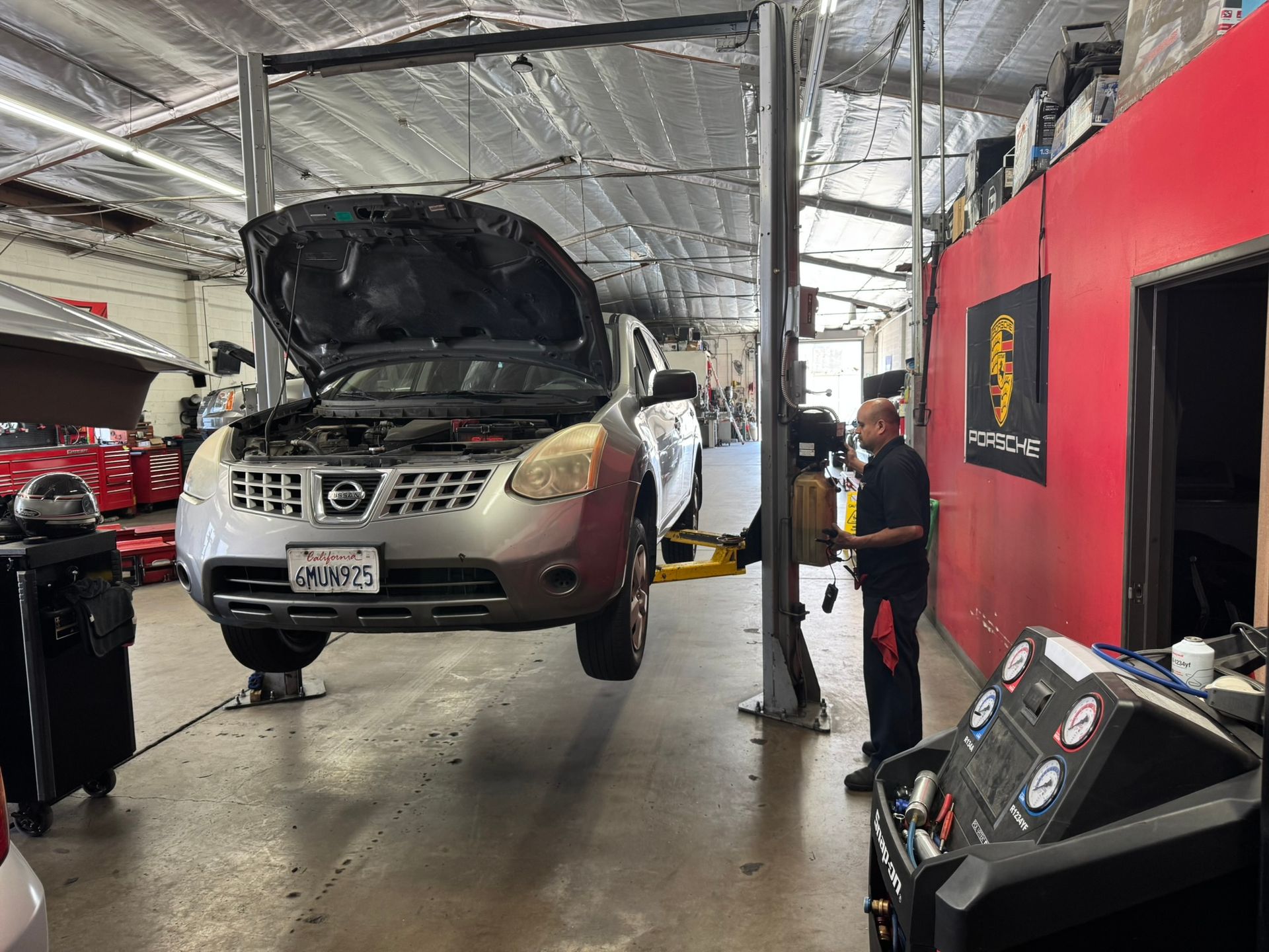 Silver SUV on a lift in a garage, hood open, with mechanics nearby and tools on the floor.