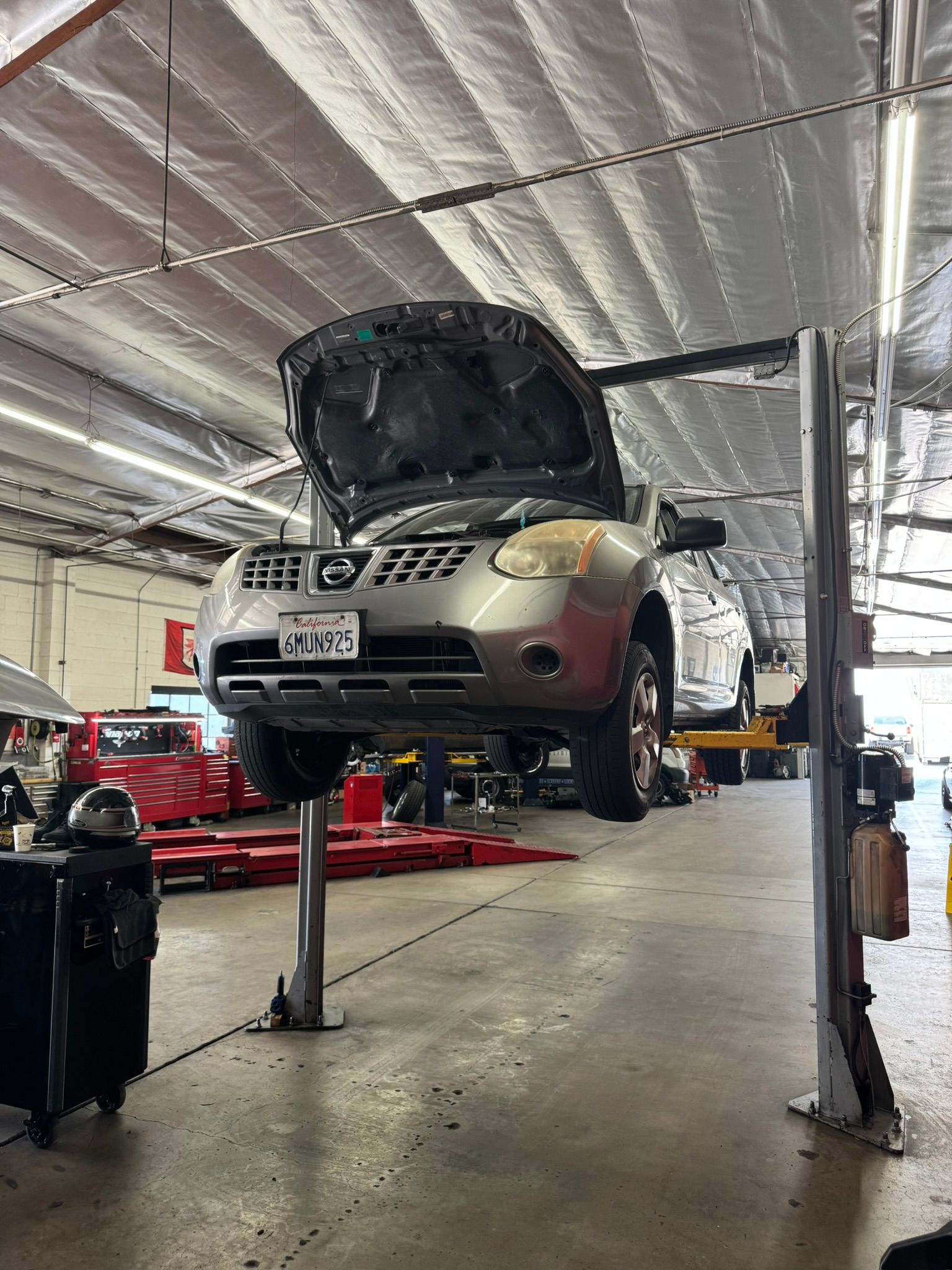 Car raised on a lift in an auto repair shop with its hood open and front bumper removed