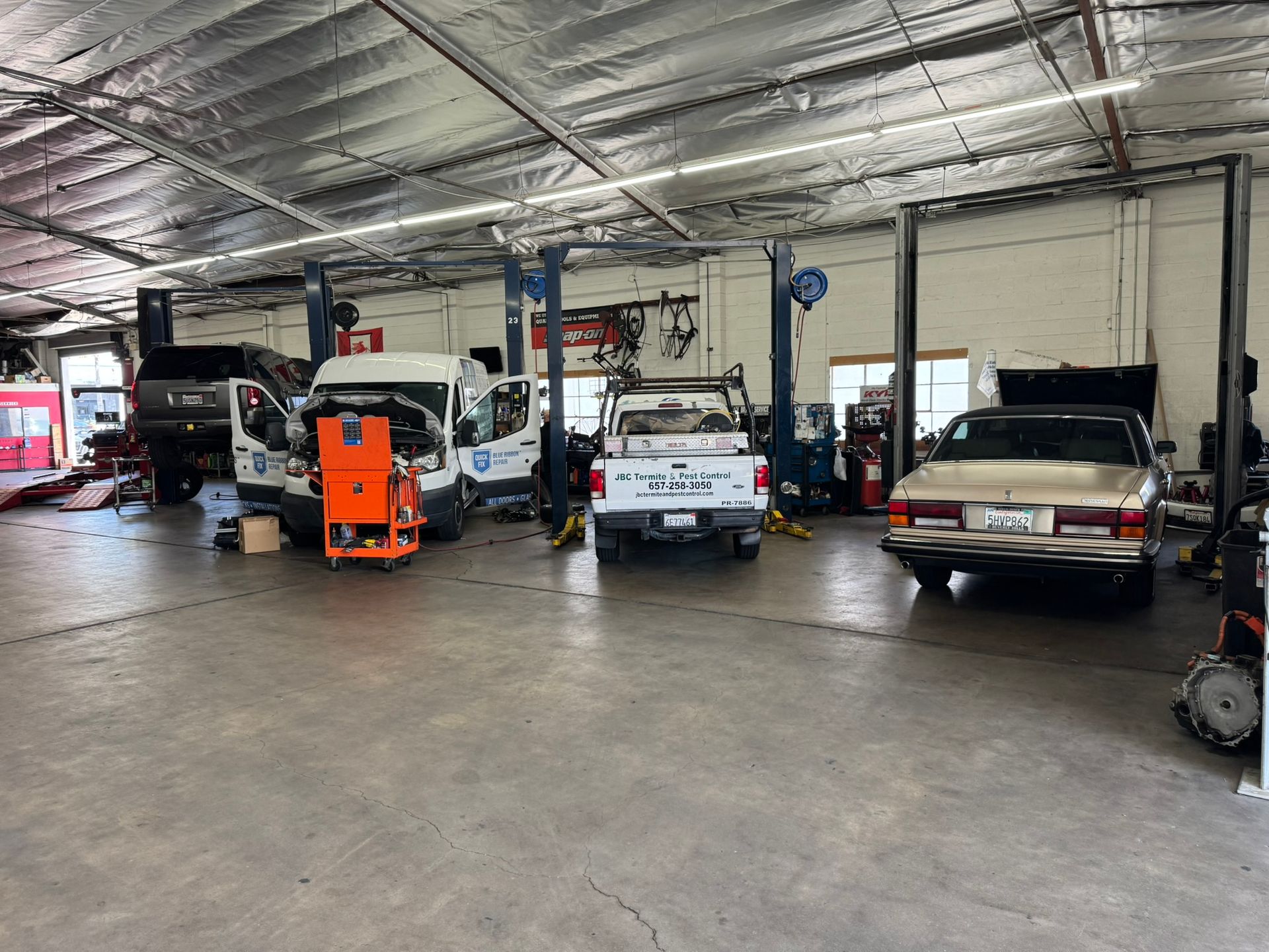 Auto repair shop with several vehicles parked inside, including a van, forklift, and pickup truck.