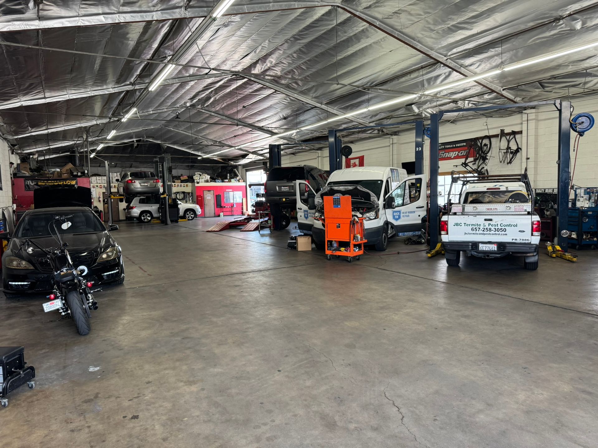 Auto repair garage with vehicles, a red car, and an orange lift in a large workshop