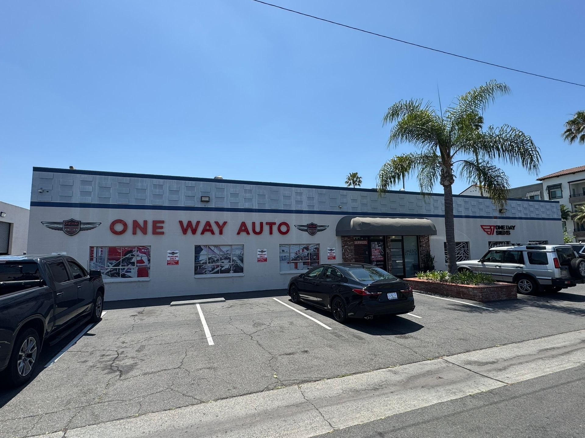 One Way Auto storefront with parked cars under a clear blue sky.
