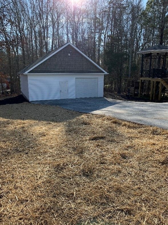 A white garage is sitting in the middle of a grassy field.