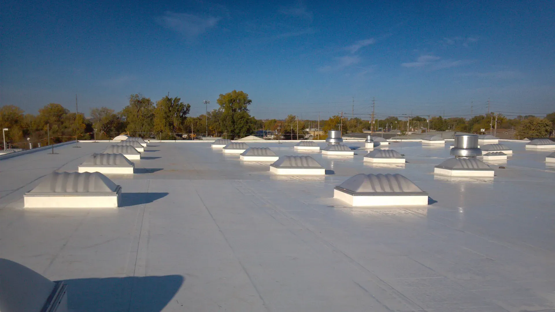 White flat roof with skylights under a clear blue sky.