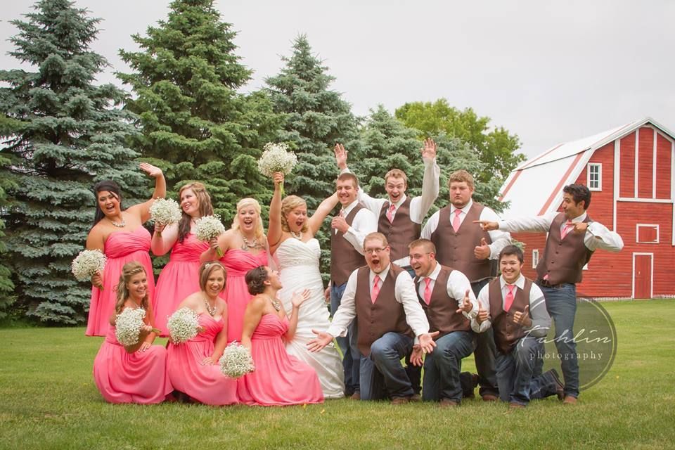 A bride and her wedding party are posing for a picture in front of a red barn.