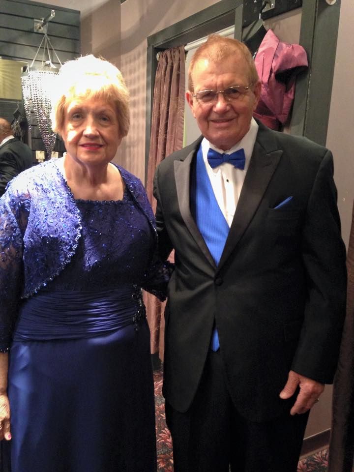 A man in a tuxedo stands next to a woman in a blue dress