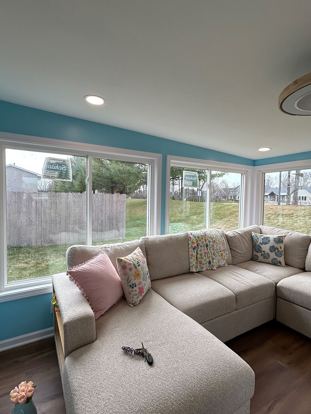 A beige sectional sofa with a patterned pillow, a pink pillow, and a small toy gun sits in a bright room with blue walls.