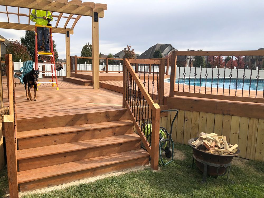 A gray wooden deck and stairs lead up to an above-ground swimming pool in a residential backyard.