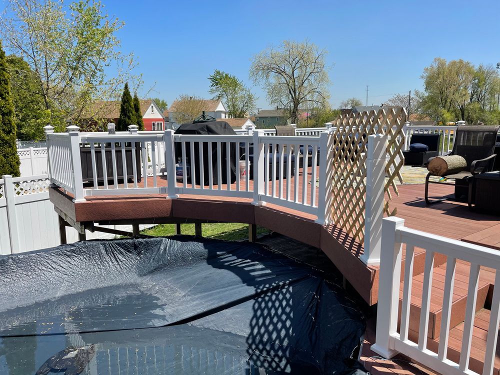 An elevated red composite deck with white railings overlooks a pool covered by a black solar blanket on a sunny day.