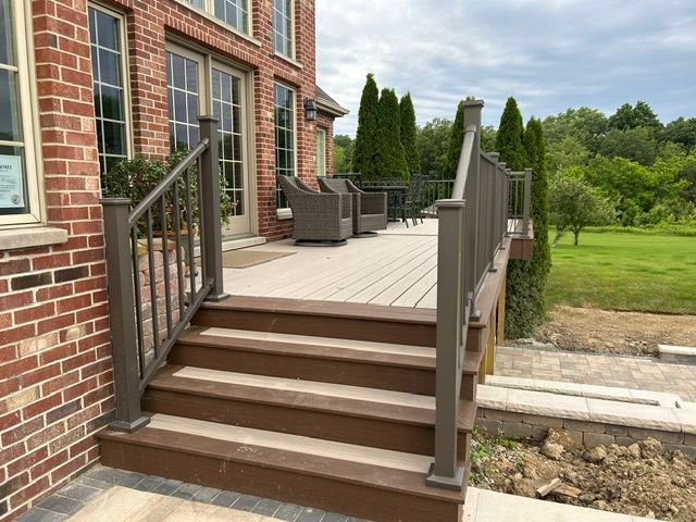 Wooden deck steps with railings beside a brick house, overlooking a green yard.