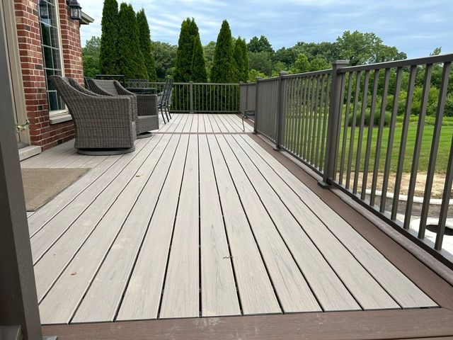 Spacious deck with gray planks, wicker chairs, and black railing overlooking a green yard