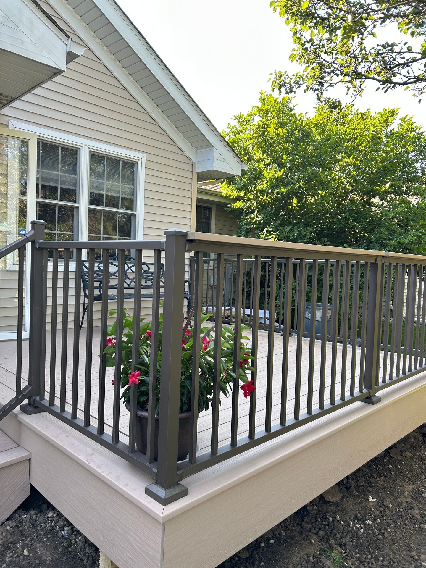 House deck with gray metal railing, beige siding, and potted flowers beside a window