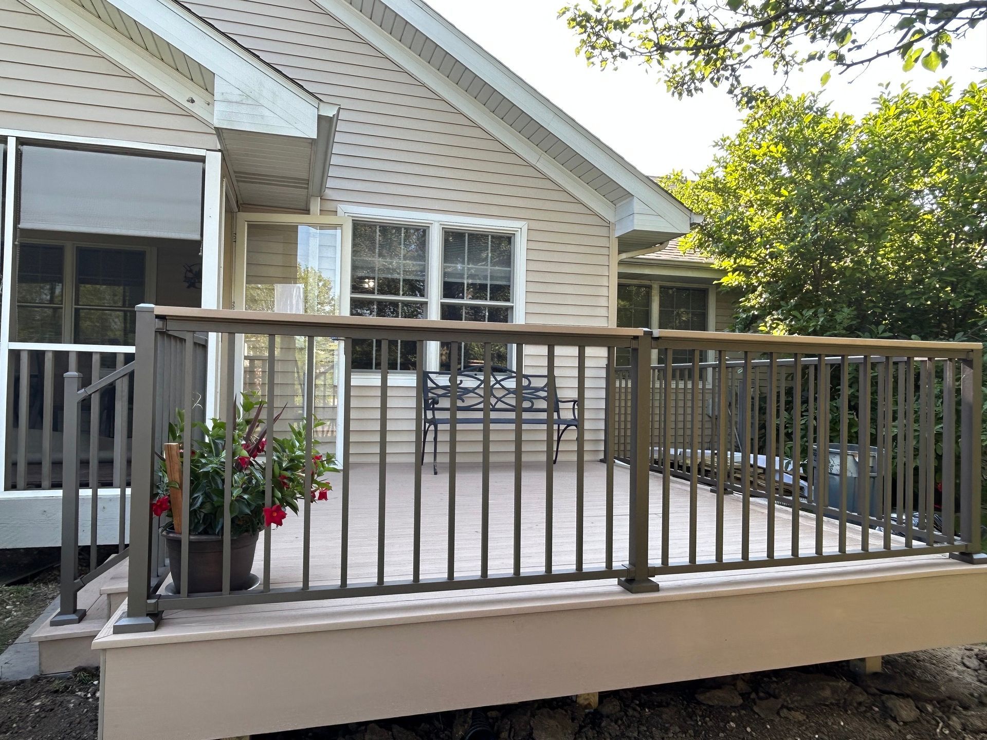 Back deck with gray railing, potted flowers, and patio chairs beside a beige house