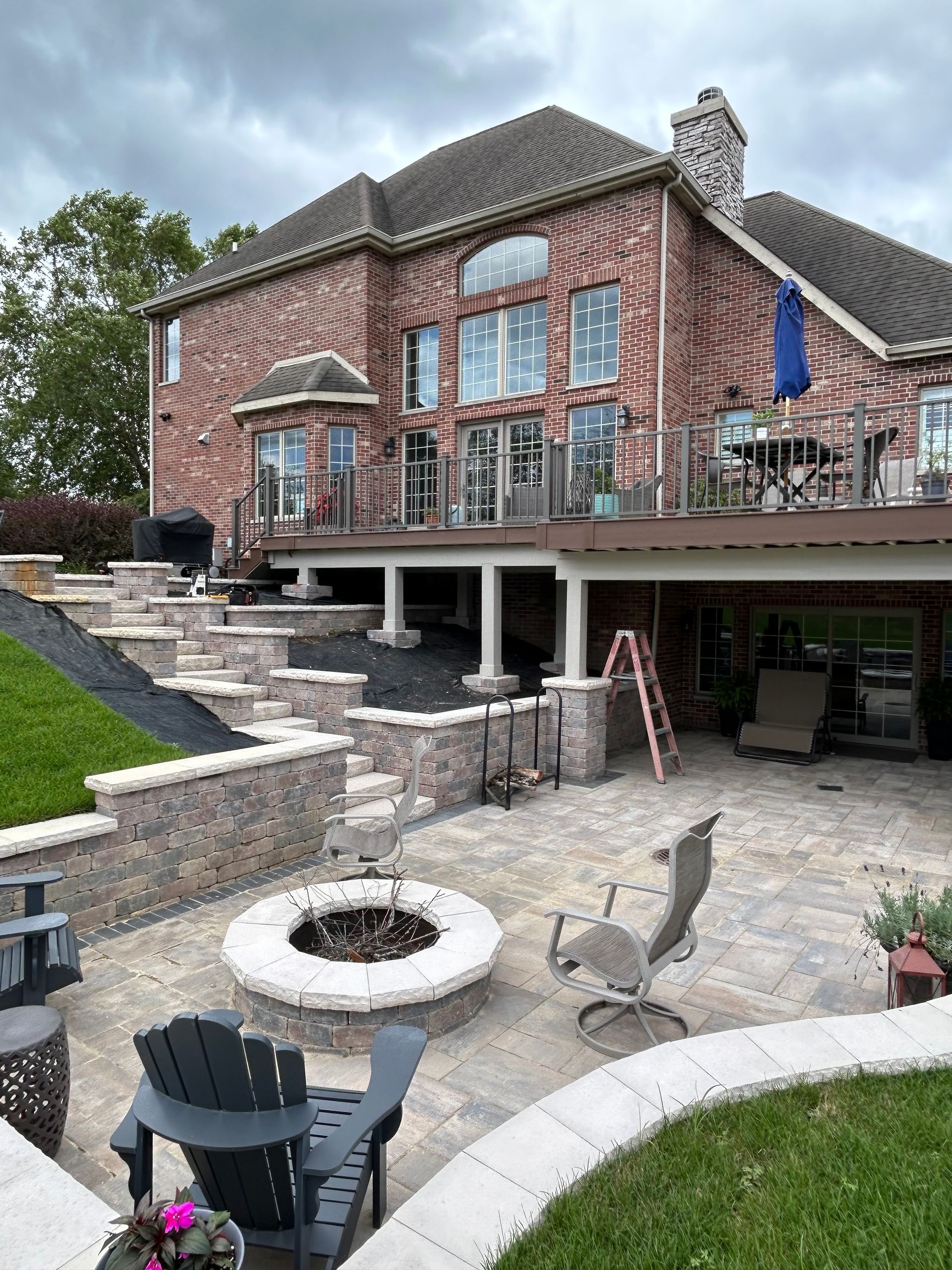 Brick house patio with stone fire pit, stairs, outdoor chairs, and large windows overlooking the yard