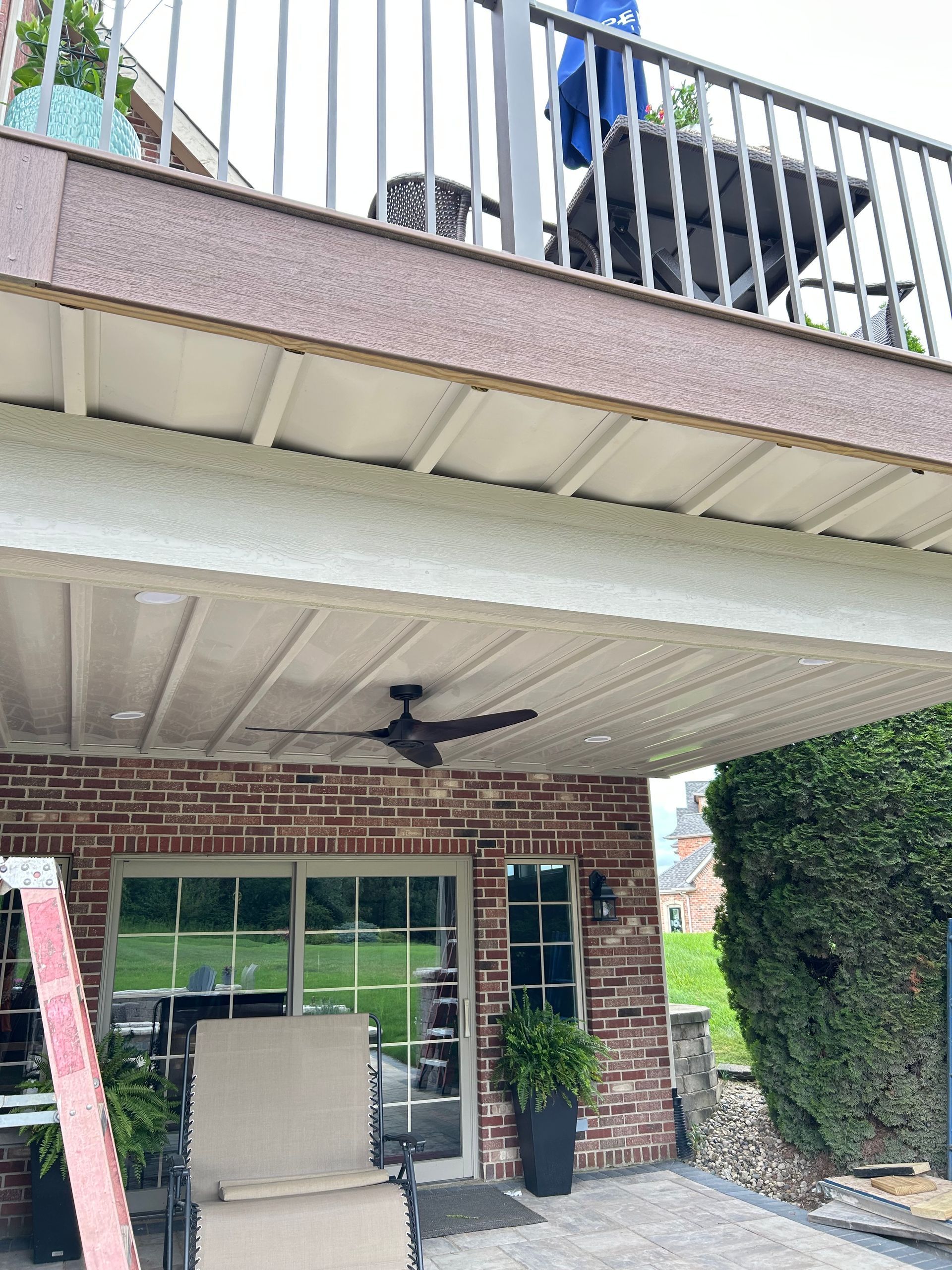 Patio under a balcony with ceiling fan, brick wall, glass door, and outdoor seating area