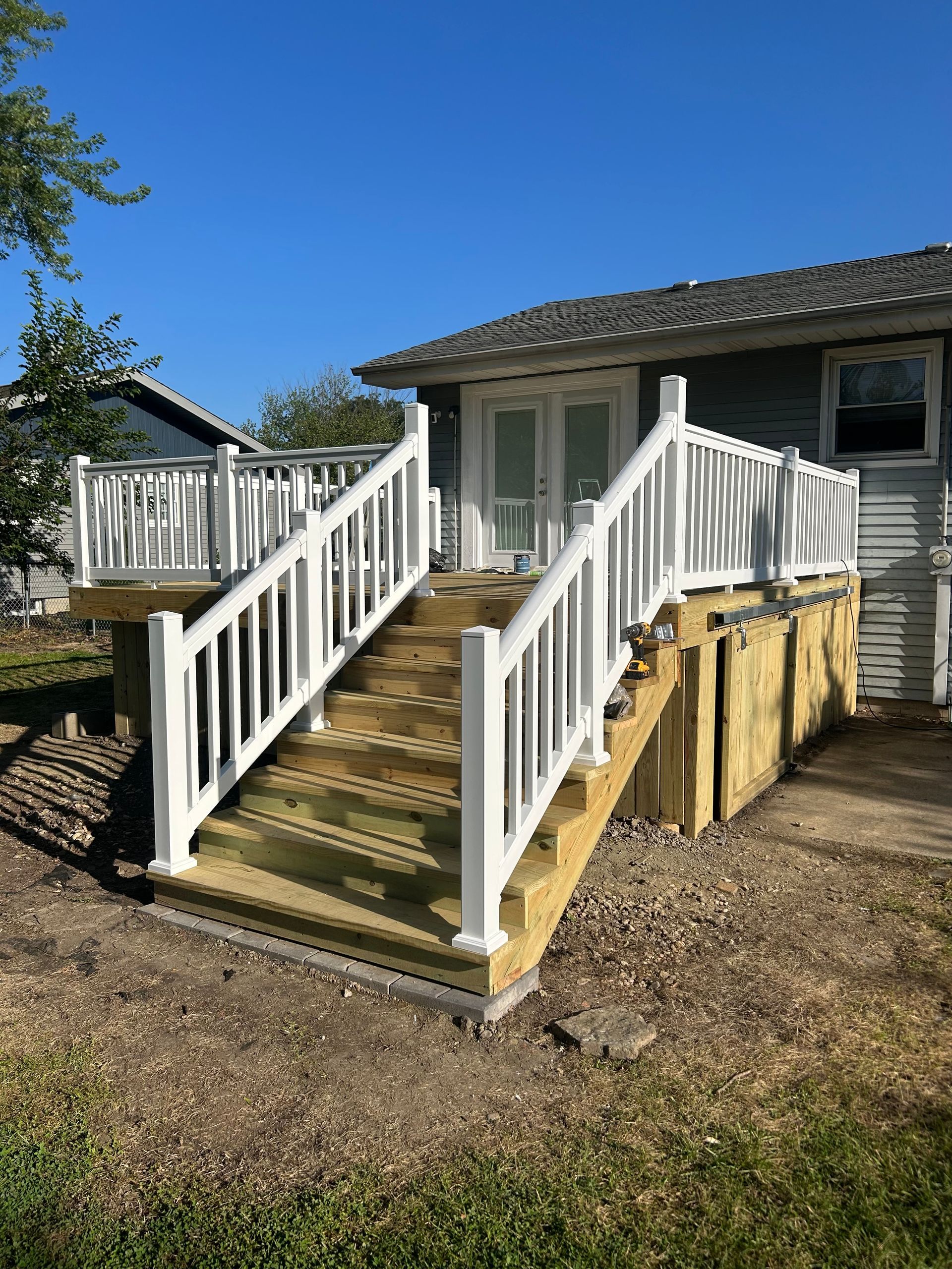 A wooden deck with white railings and stairs leading up to the back glass doors of a house under a clear blue sky.
