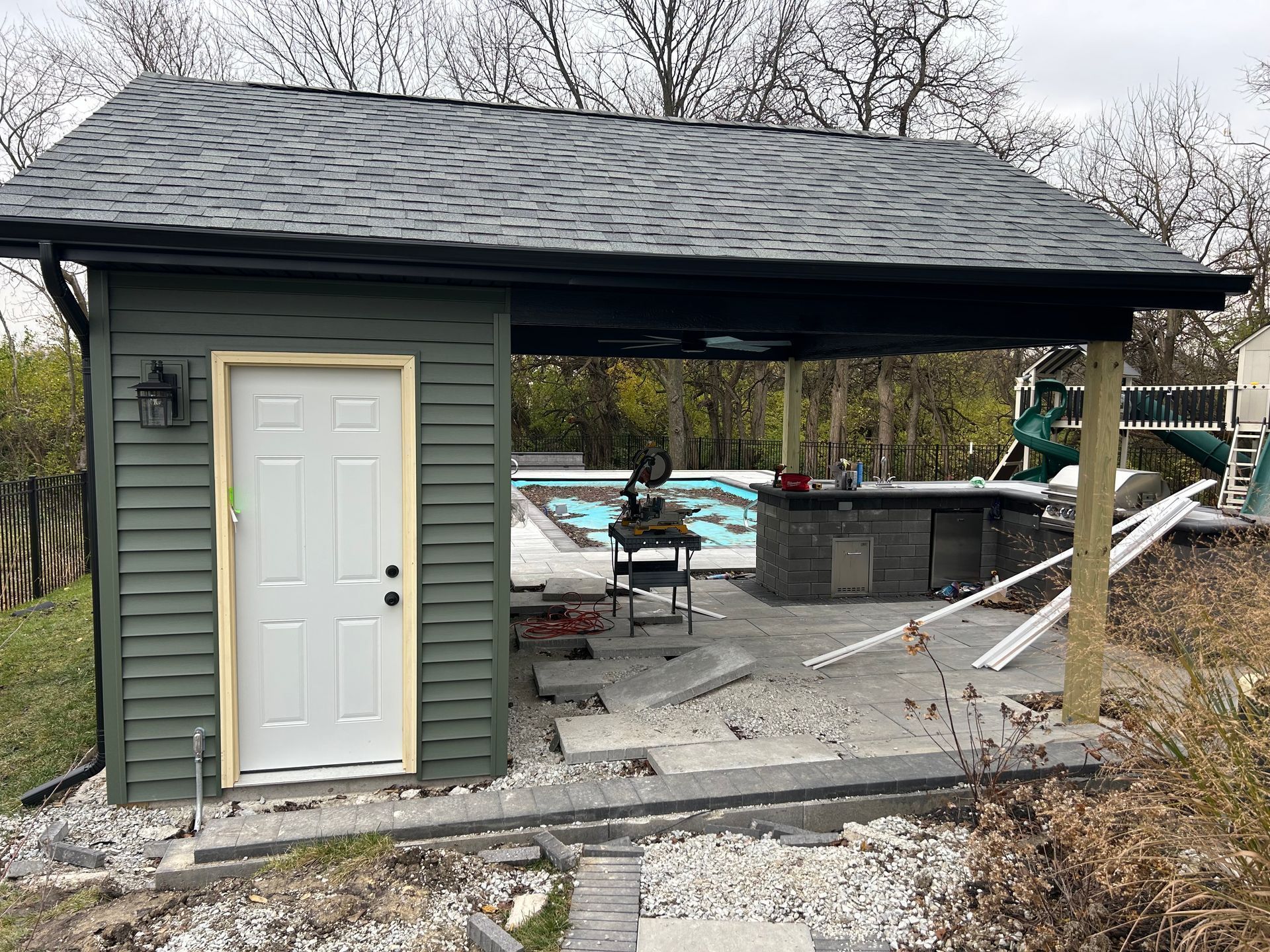 Small gray shed with white door and covered patio, damaged concrete and debris around it