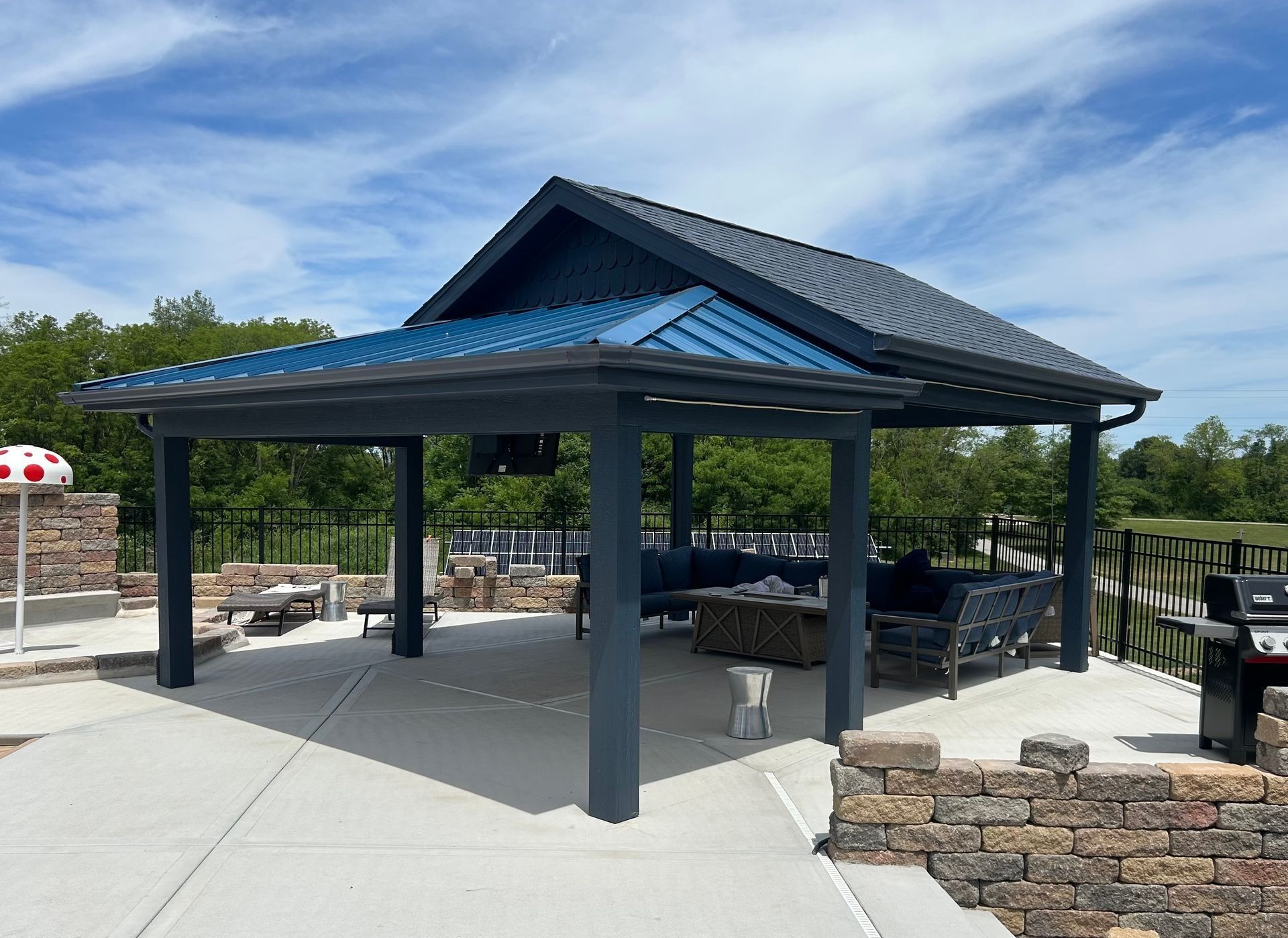 Blue-roofed park pavilion with picnic tables and stone landscaping under a clear sky
