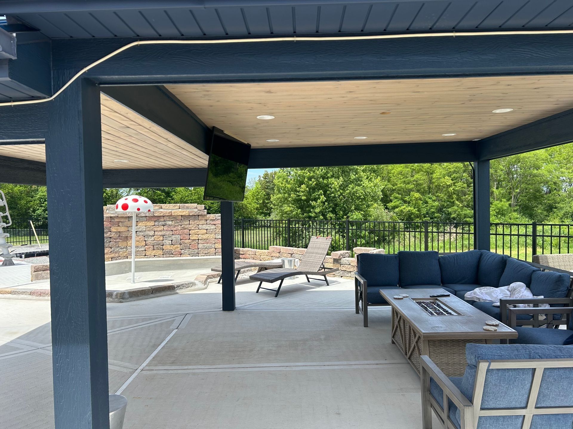Covered outdoor patio with blue sofas, table, and a fire pit overlooking a pool and trees