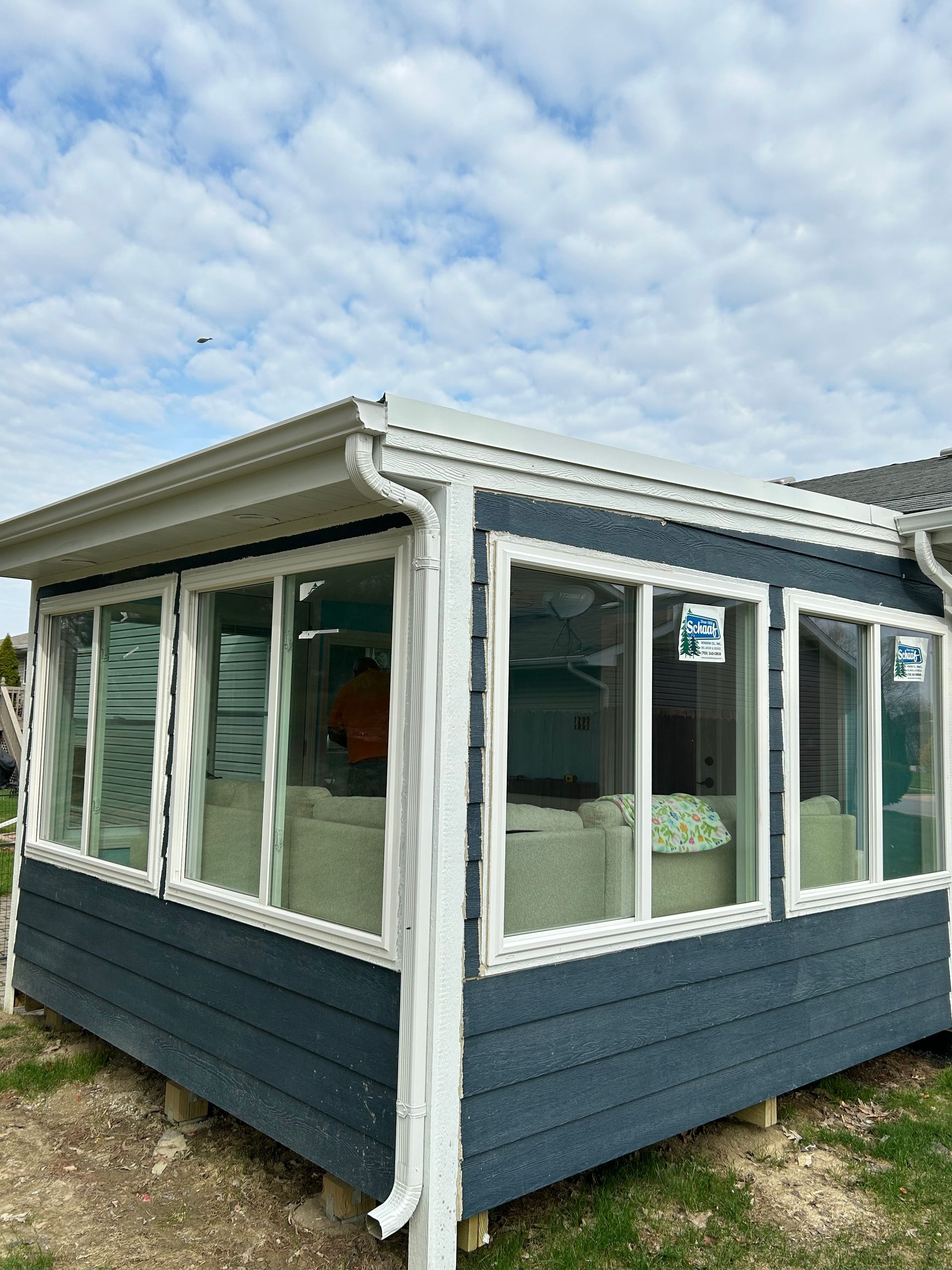 A small sunroom with dark blue horizontal siding and white-framed windows under a cloudy sky.
