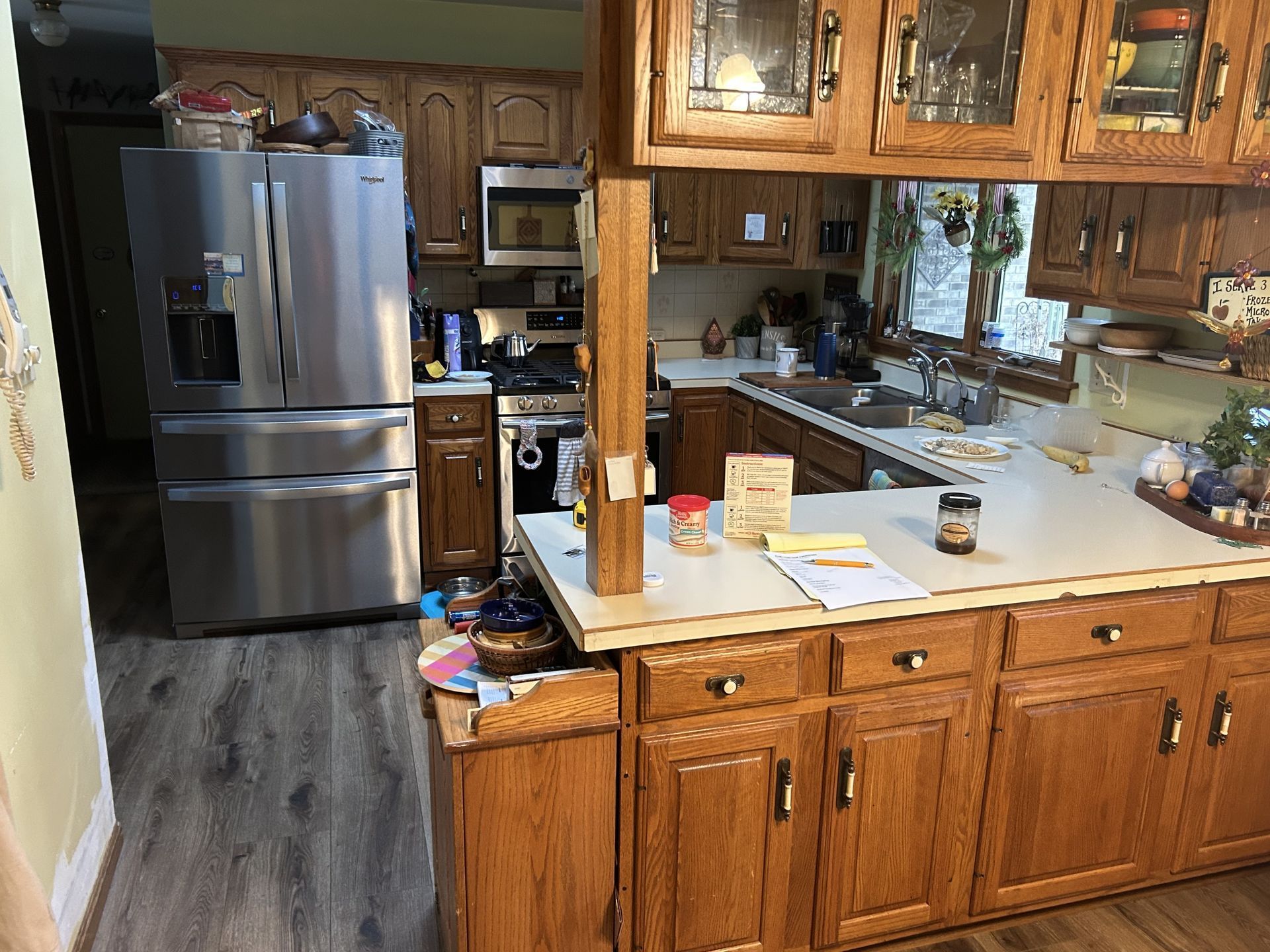 Before - Kitchen with wooden cabinets, stainless steel refrigerator, and countertop with items.
