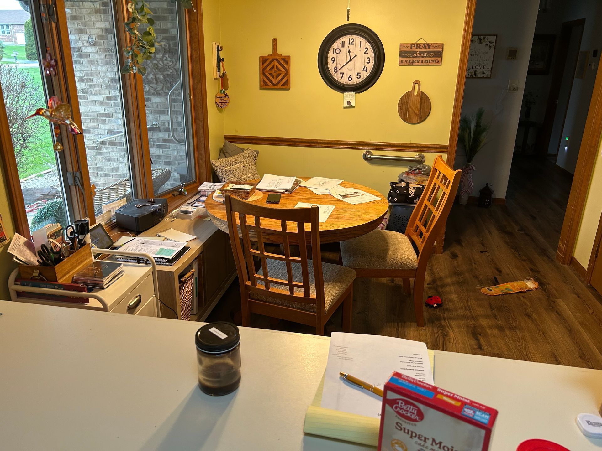 Before - A kitchen with a round table, chairs, a window, and a clock on the wall. A counter is in the foreground.