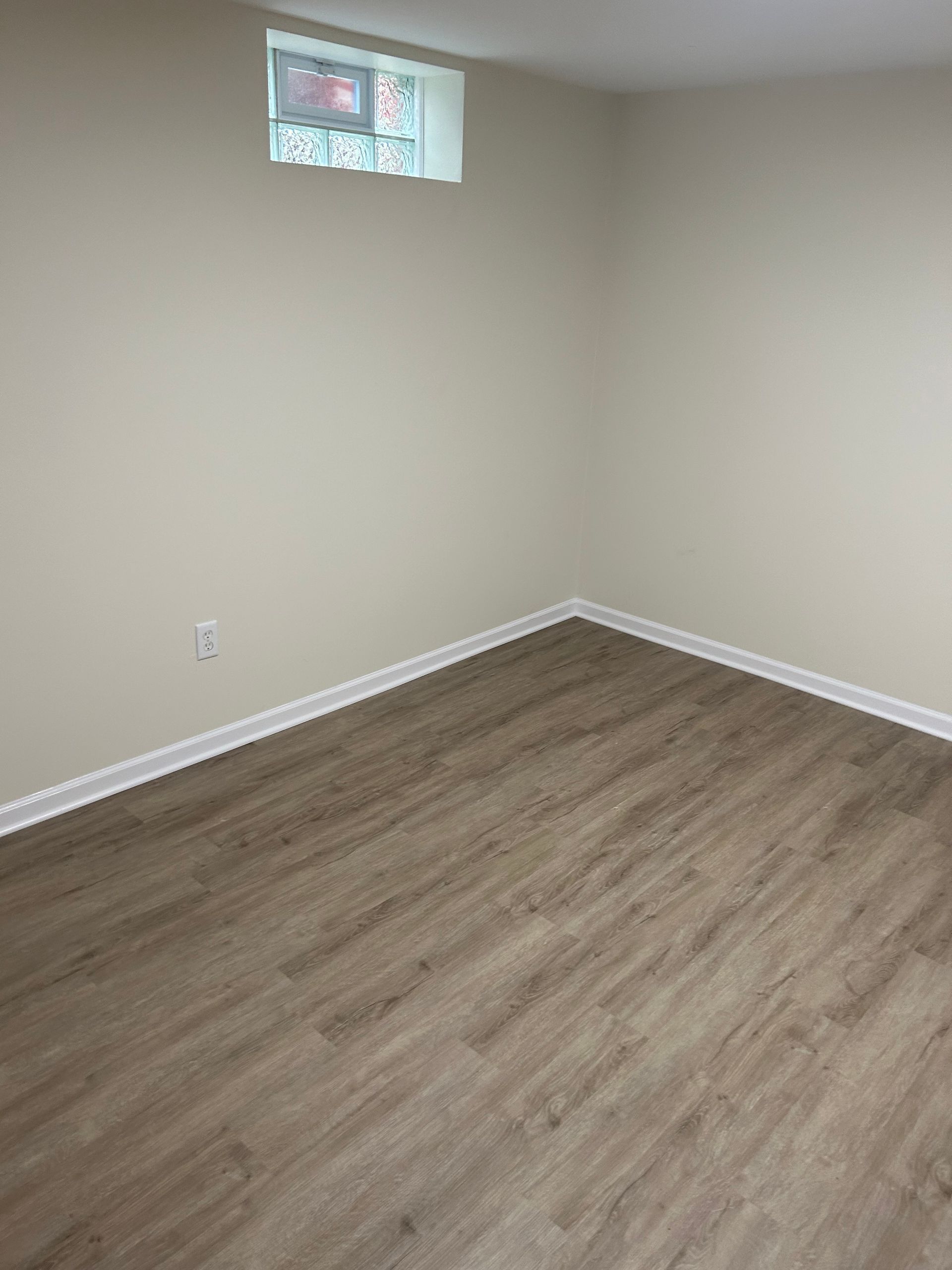 Empty room with light wood-look floor, tan walls, small window, white trim.