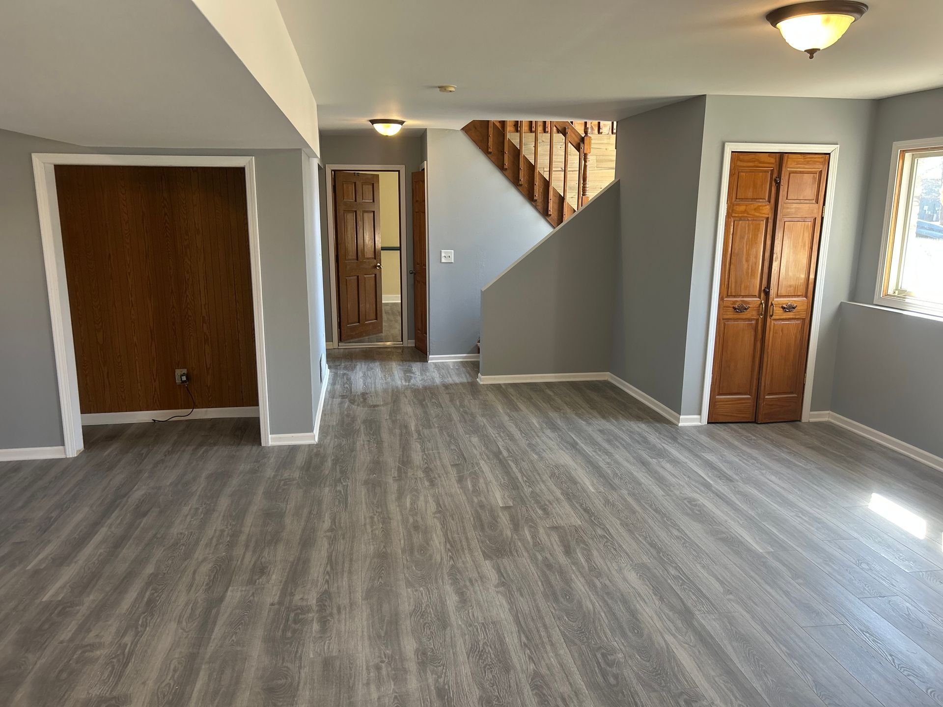 Empty room with gray flooring, stairs, brown doors, and wood-paneled wall.