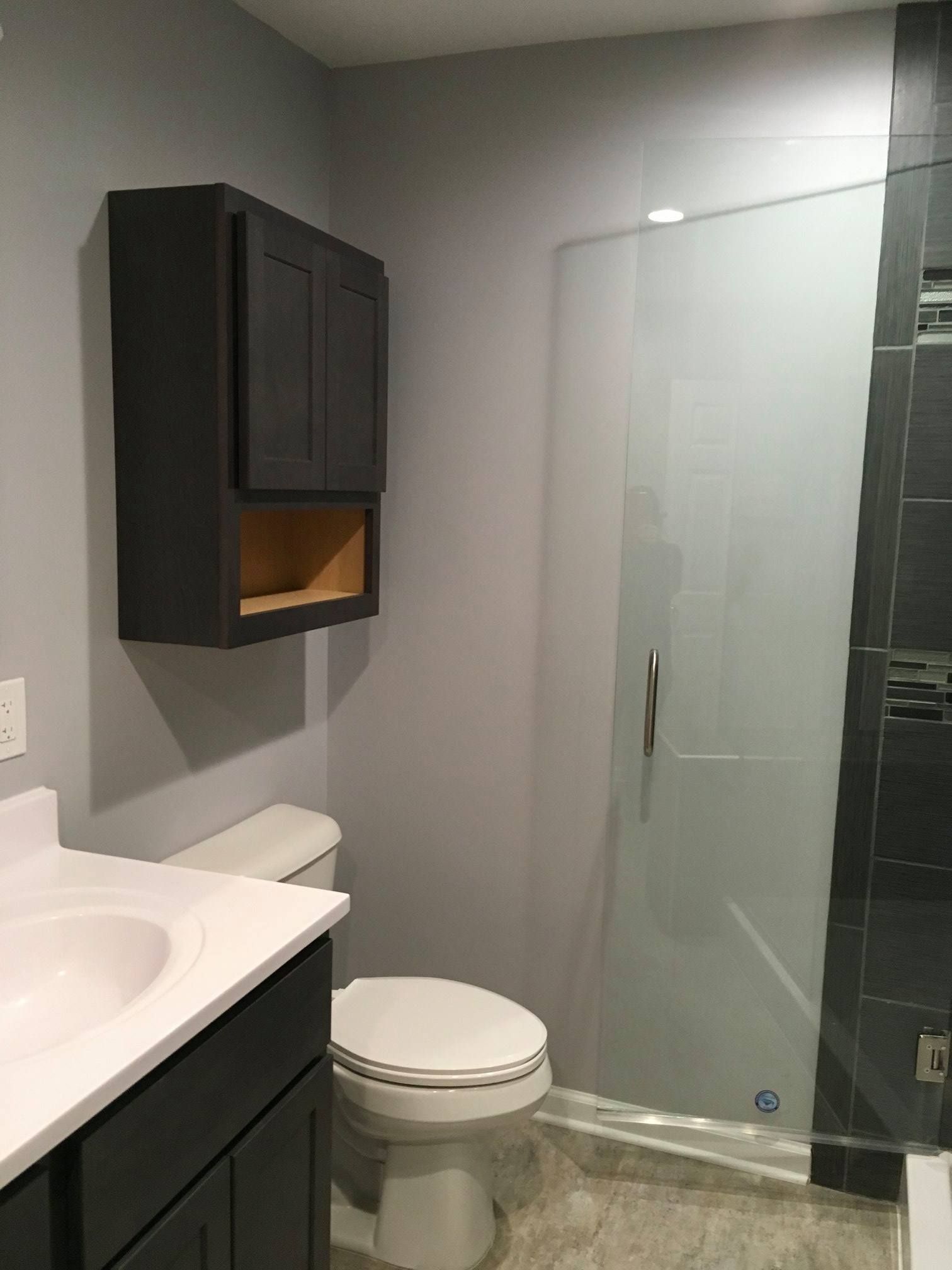 Bathroom with gray walls, dark cabinet, white toilet, glass shower door.