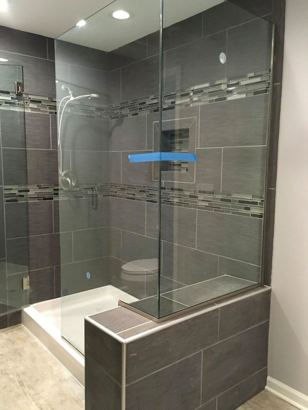 Modern shower enclosure with glass walls and gray tile, with a white shower base and toilet visible.