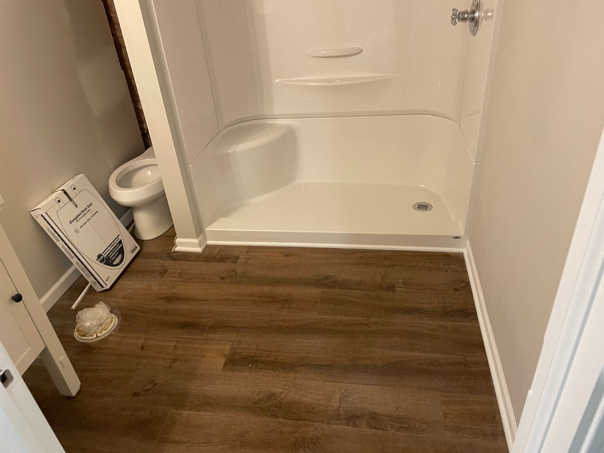 Bathroom with white shower/tub, toilet, and brown flooring.