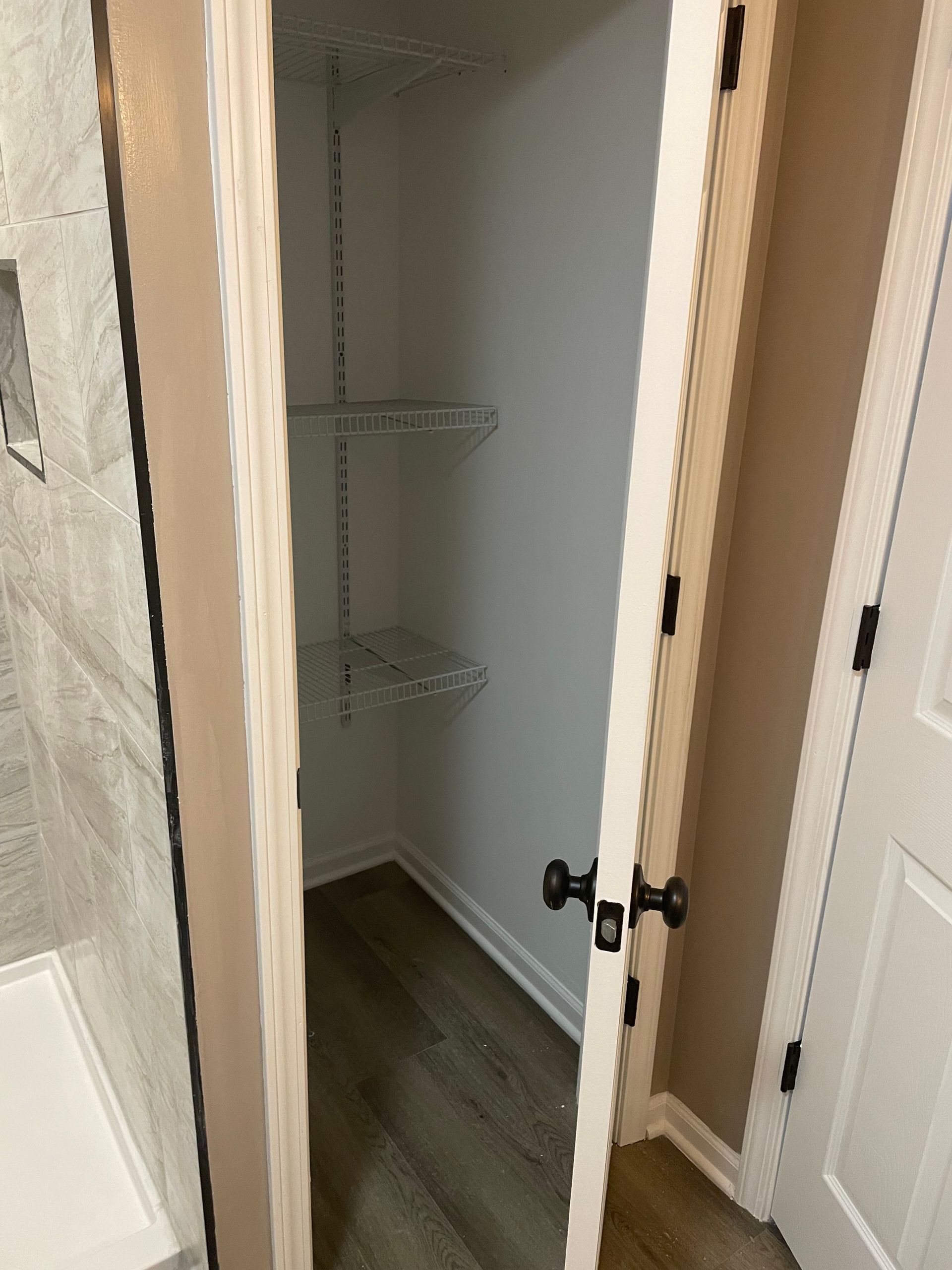 Open white closet with wire shelves and dark door handles.