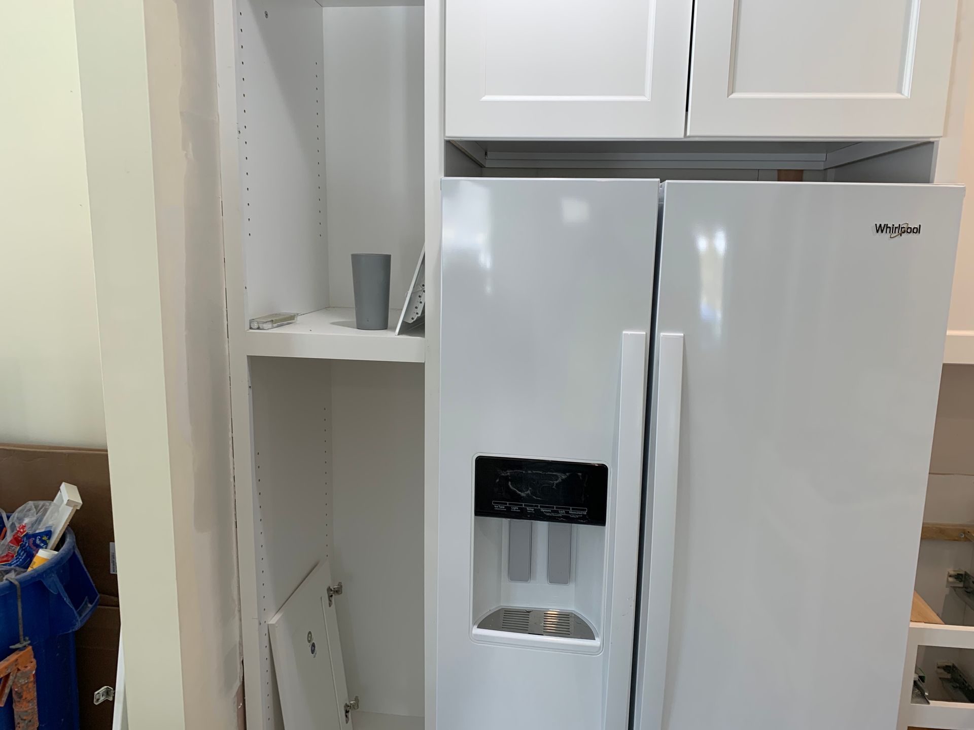 White Whirlpool refrigerator installed in a kitchen cabinet, with additional cabinetry above.