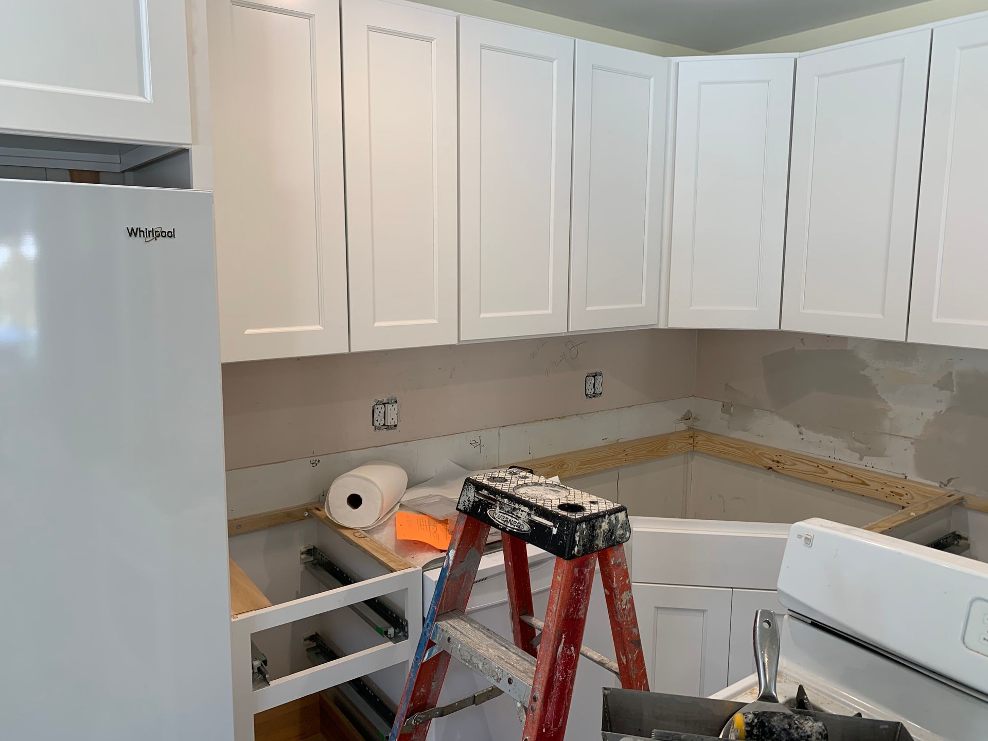 Kitchen remodel in progress: white cabinets, bare wall, stepladder, refrigerator, stove.