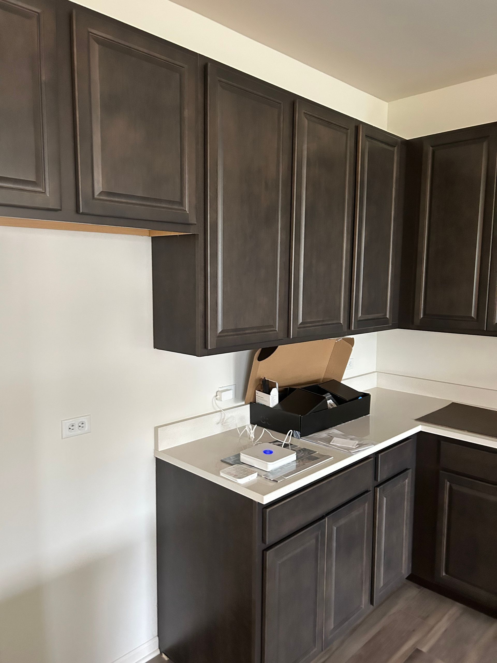Dark brown kitchen cabinets and white countertop. Unfinished wall, cardboard box, and a few items on the counter.
