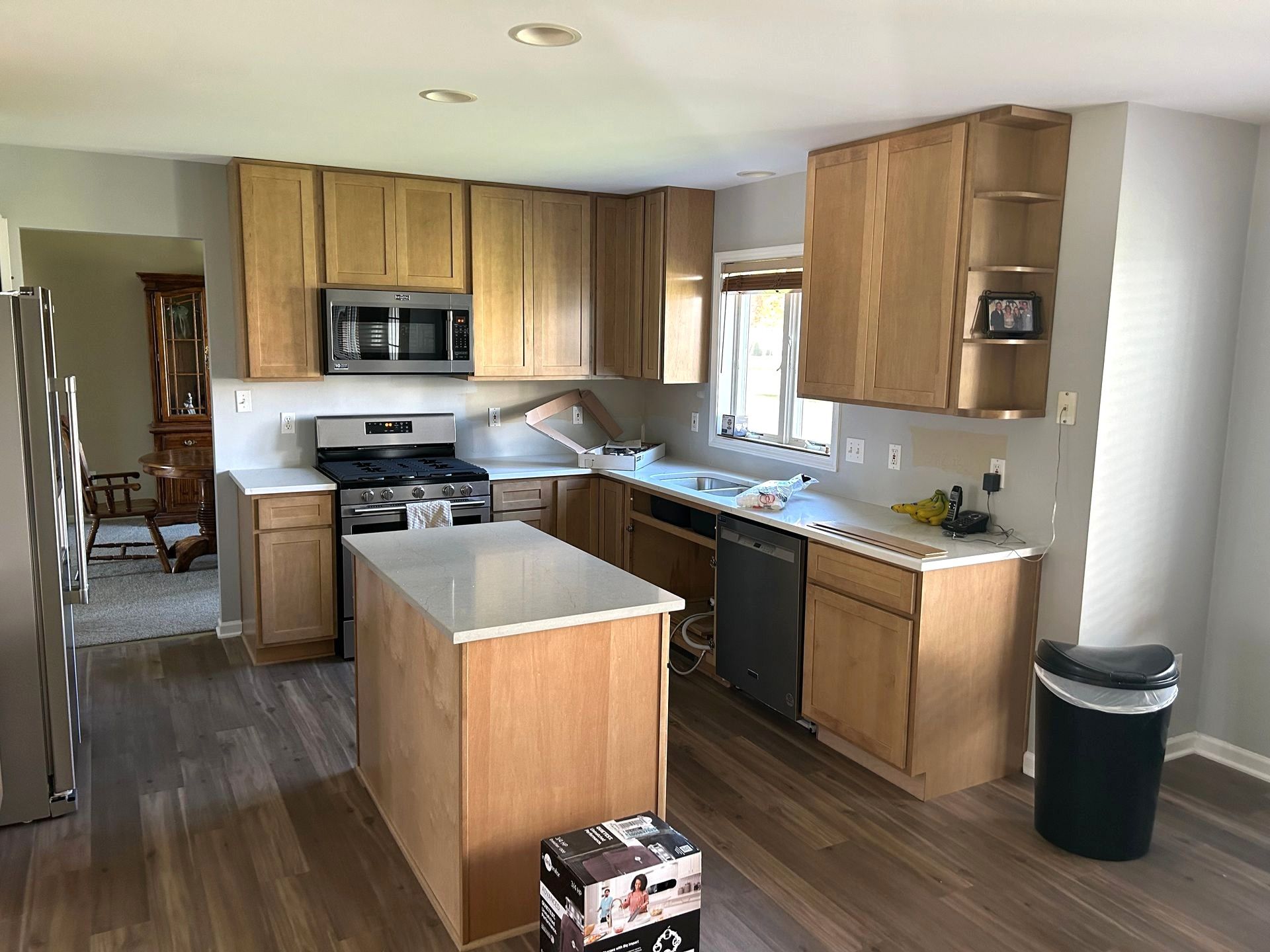 Kitchen with light wood cabinets, stainless steel appliances, and island with white countertop.