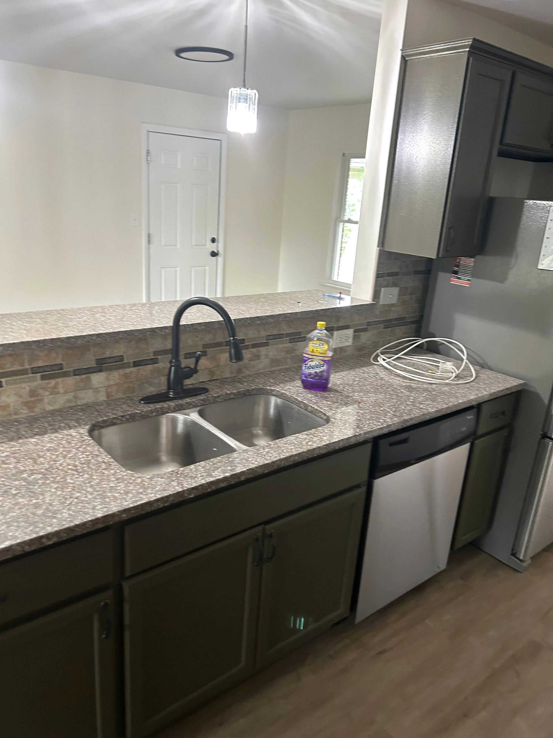 Kitchen with double sink, black faucet, granite countertop, dark cabinets, and stainless steel dishwasher.