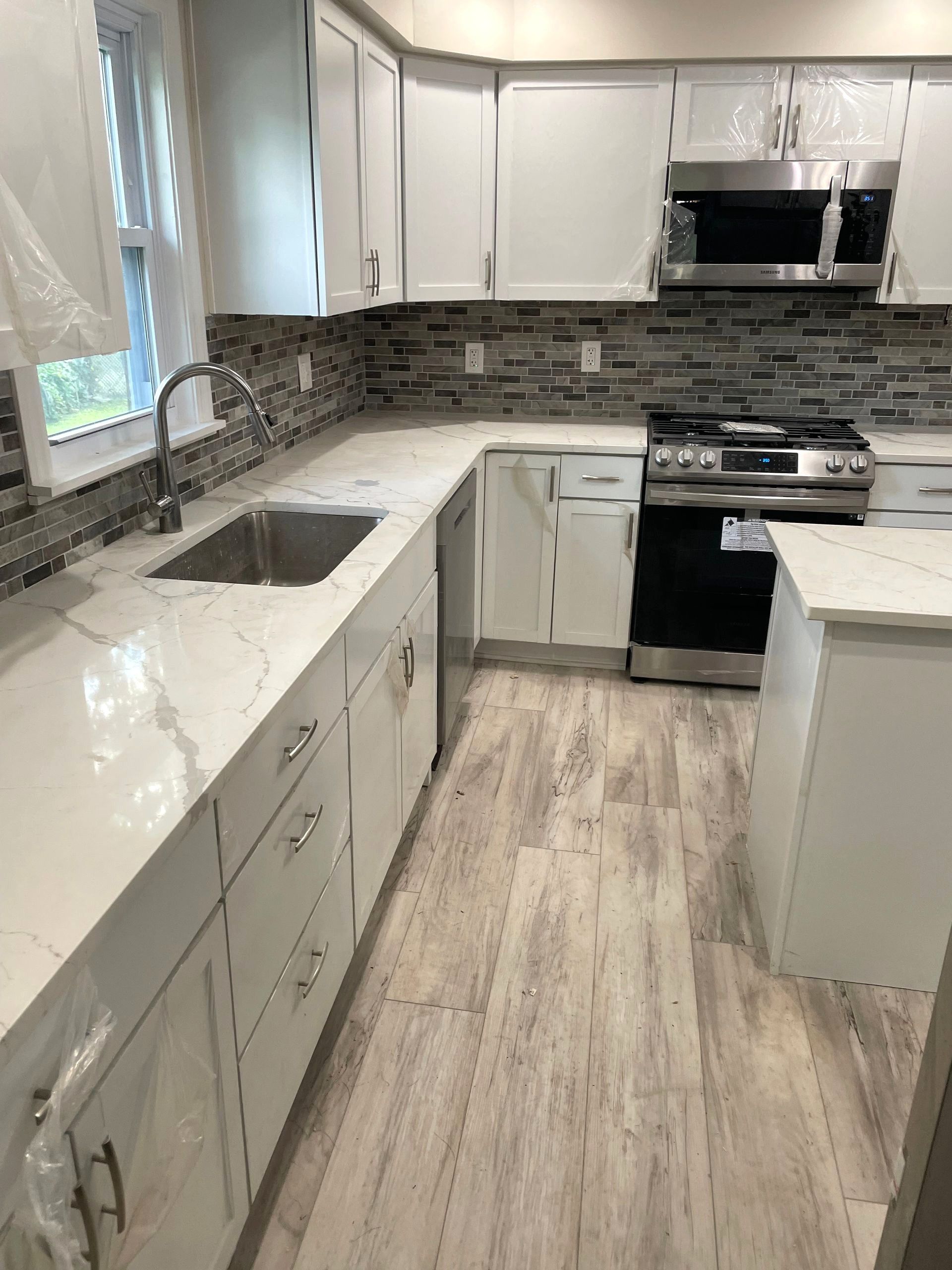 White kitchen with marble countertops, stainless steel appliances, and wood-look flooring.