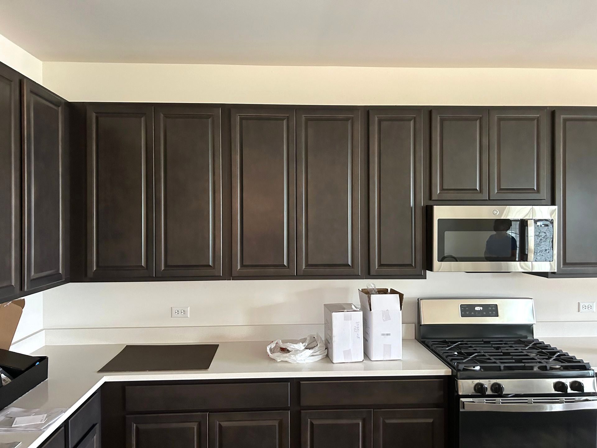Dark brown kitchen cabinets above white countertops and a stainless steel range and microwave.