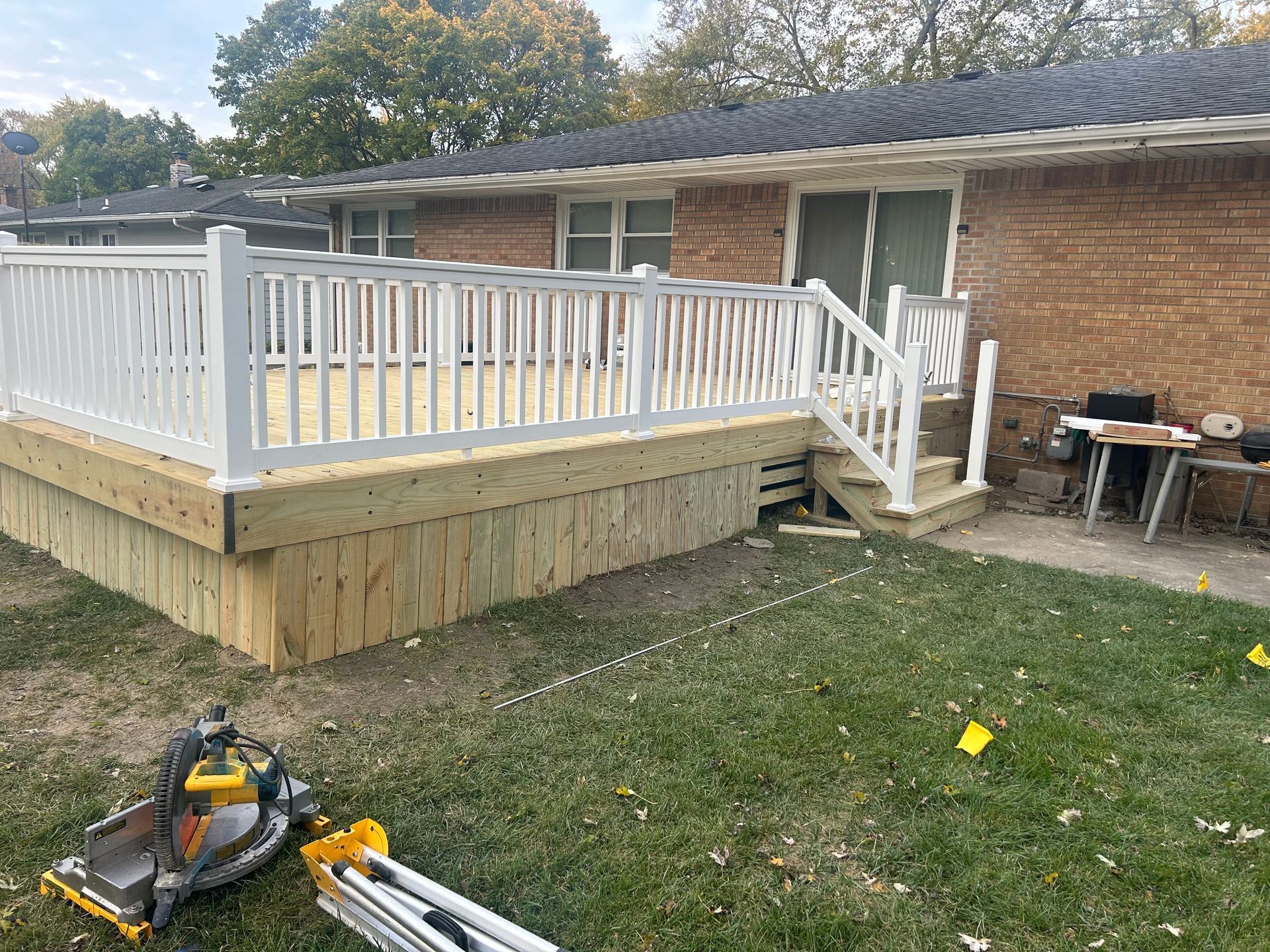 Newly constructed wooden deck with white railing, attached to a brick house, in a grassy backyard.
