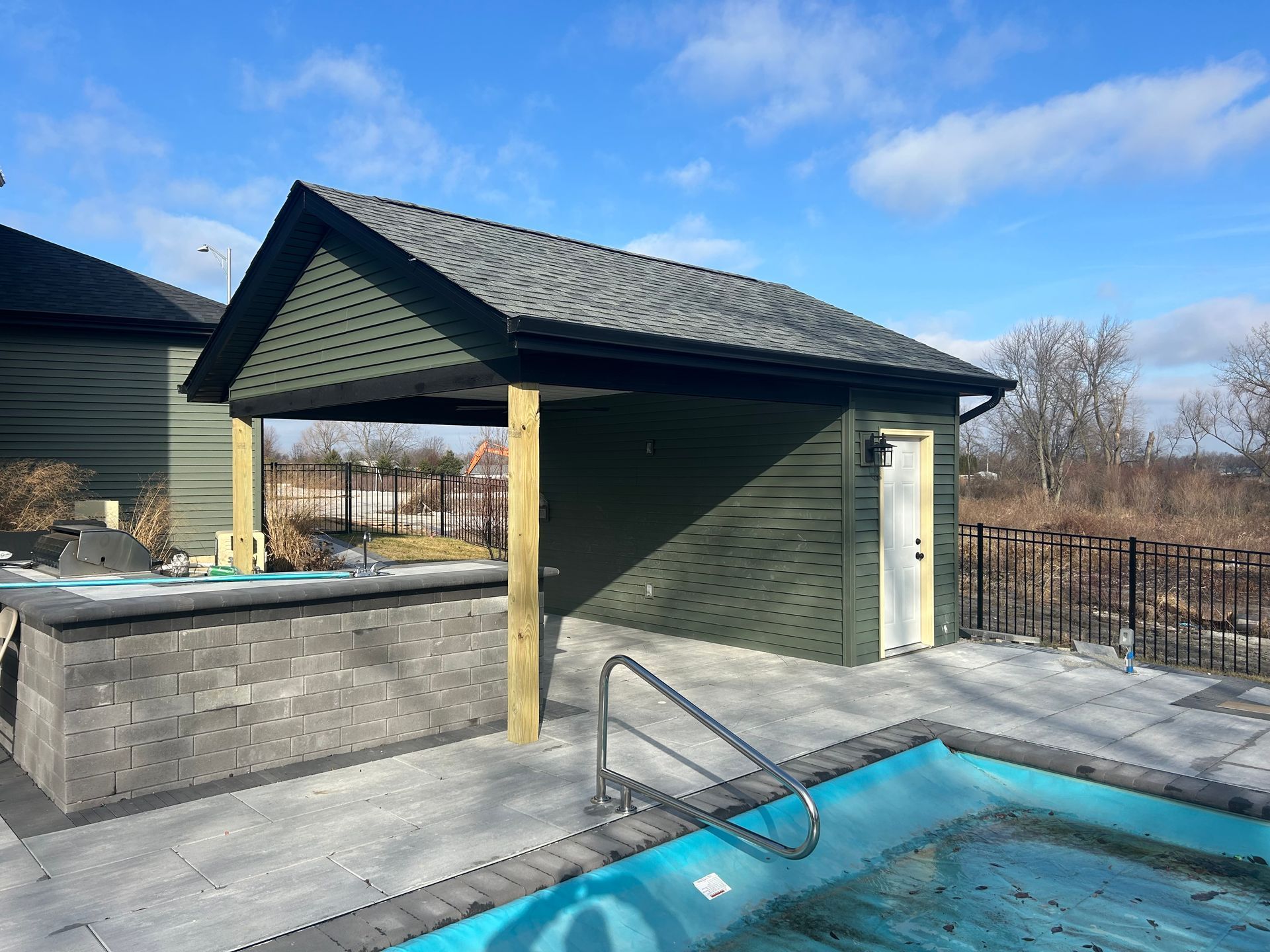 Poolside cabana with green siding, grey roof, and a built-in grill area.