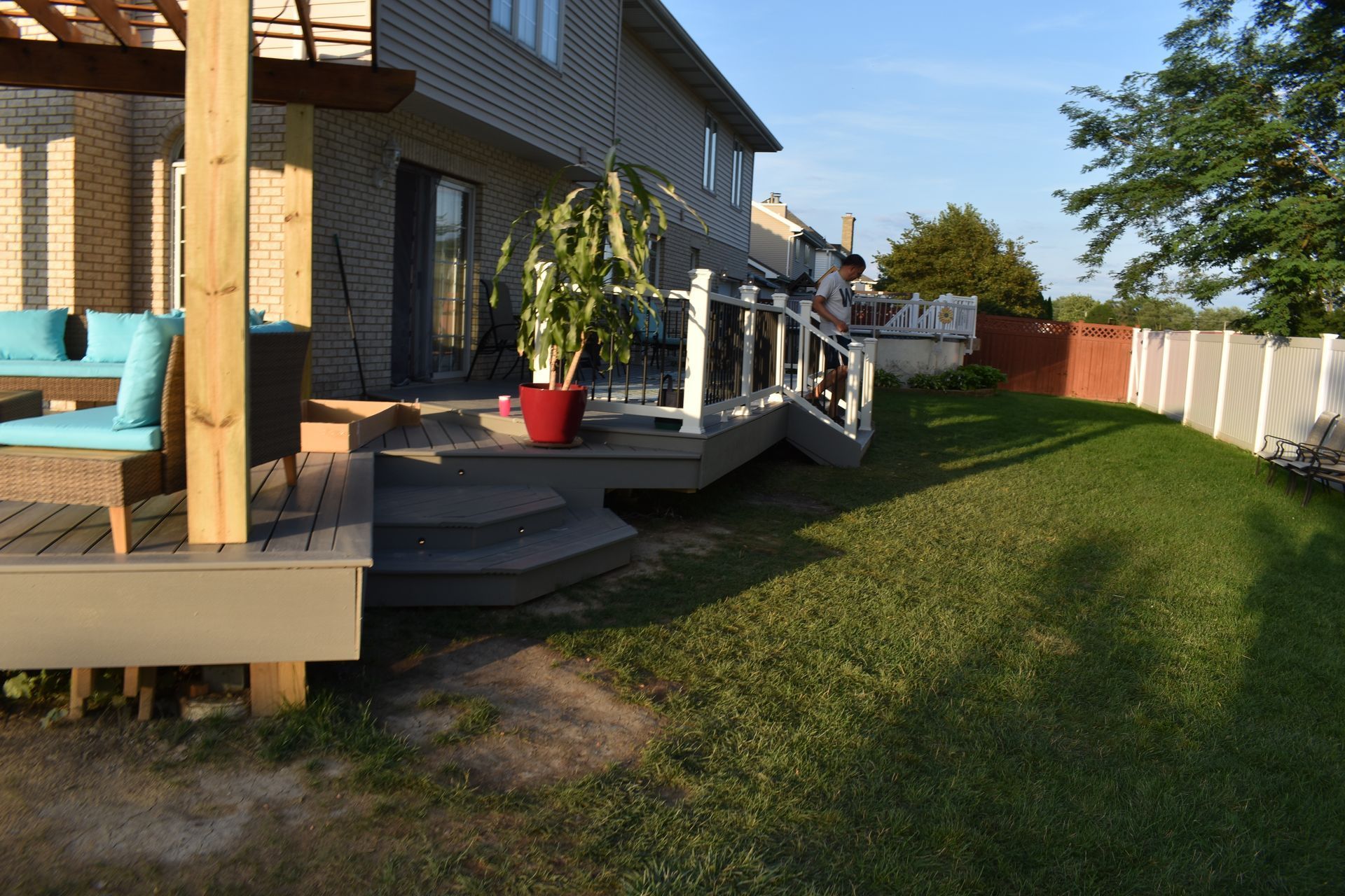 Deck with steps leading to a yard, a person on the deck, and a plant in a red pot.