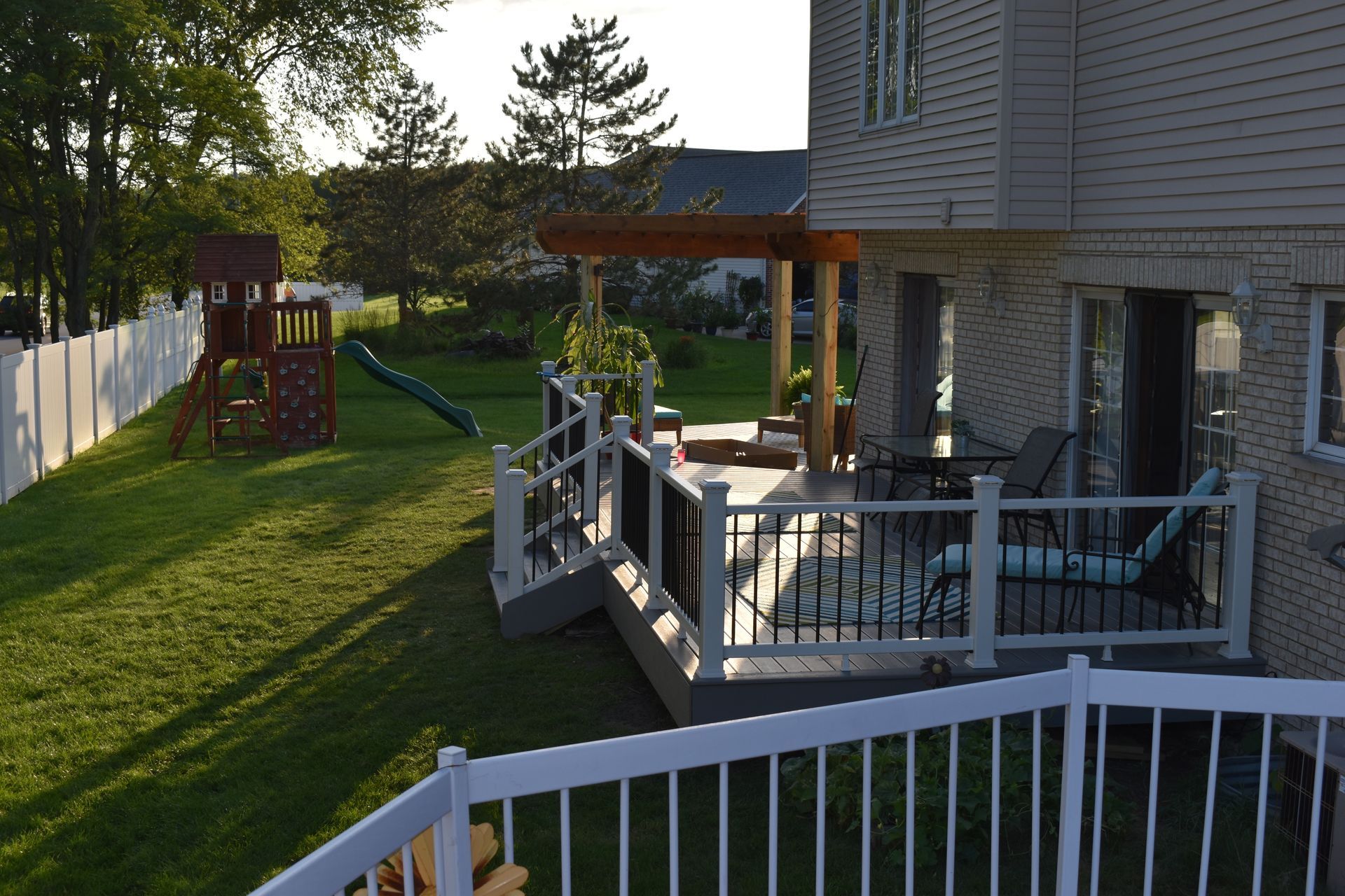 Backyard deck with pergola, overlooking a yard with a playset. White and black railings.