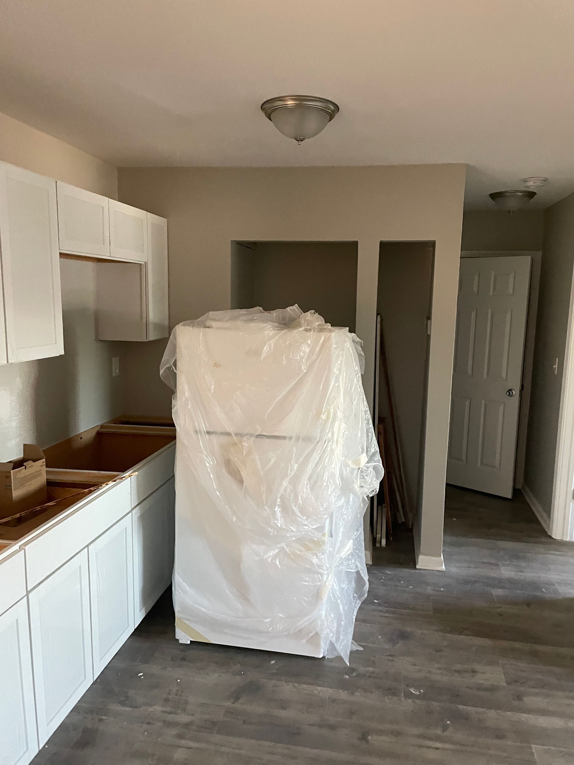 Kitchen with white cabinets, refrigerator, and door. Grey walls and flooring.