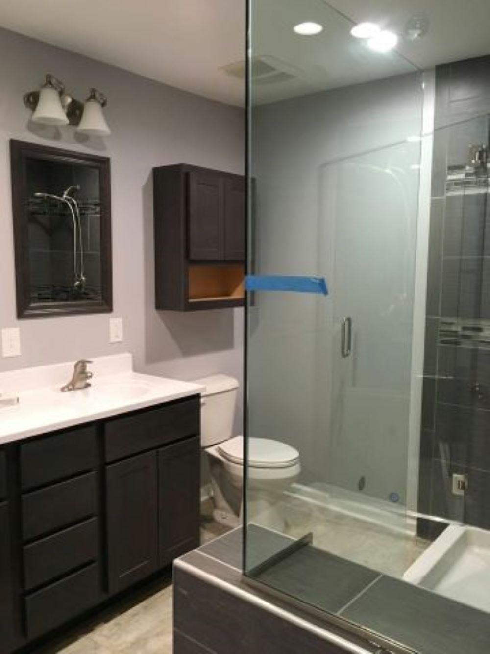 Bathroom with dark cabinetry, white countertops, glass shower, and gray walls.
