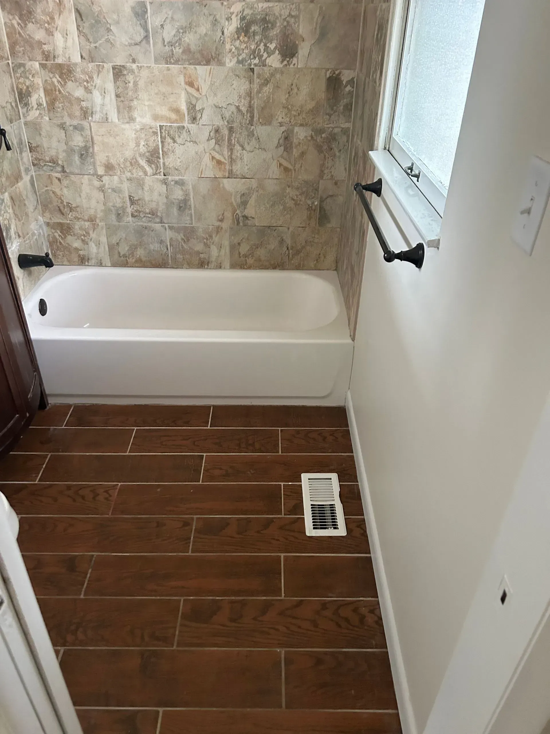 Bathroom with a white bathtub, brown tile floor, and light brown wall tiles.