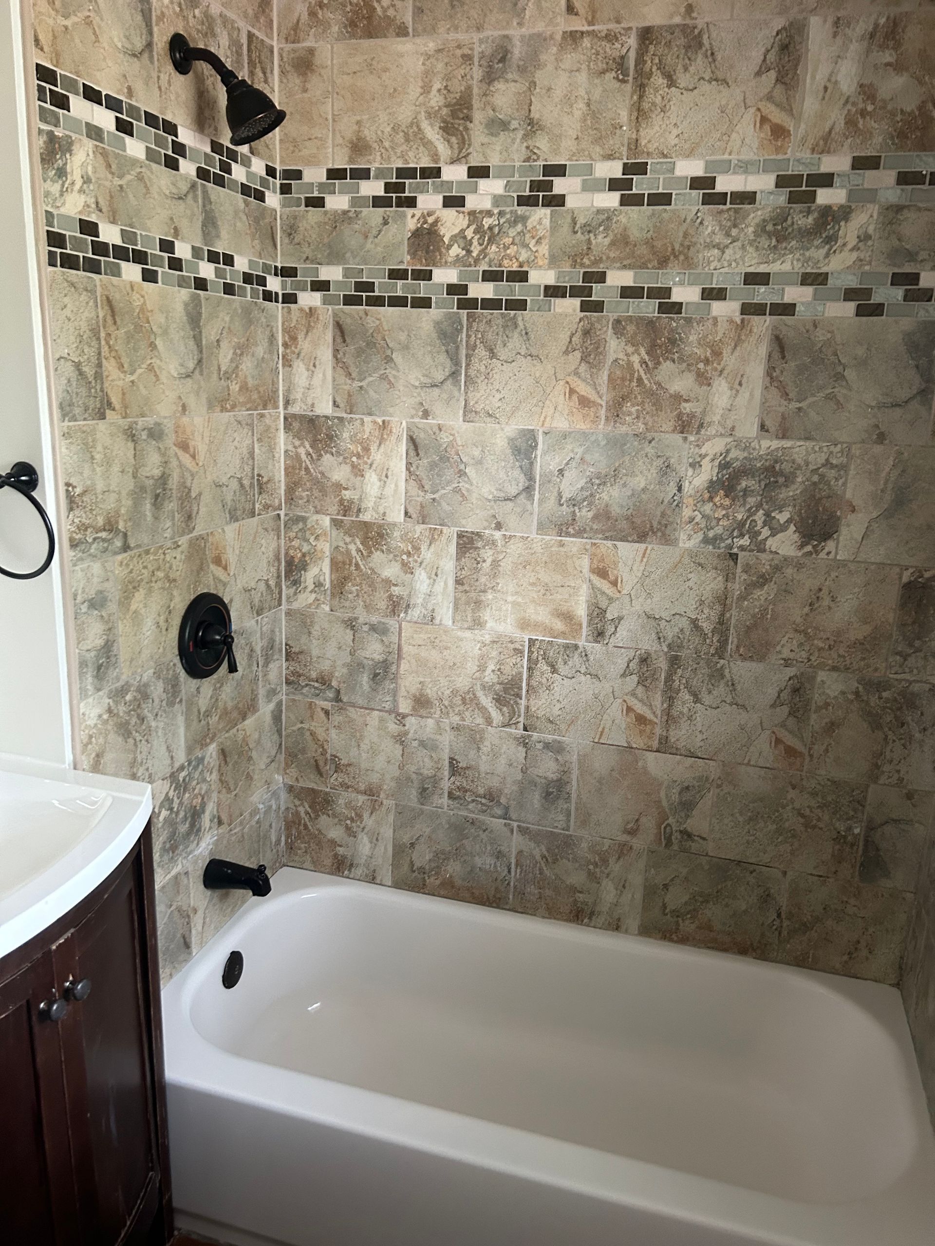 Bathroom with a white bathtub, brown and tan tile walls, and a black showerhead.